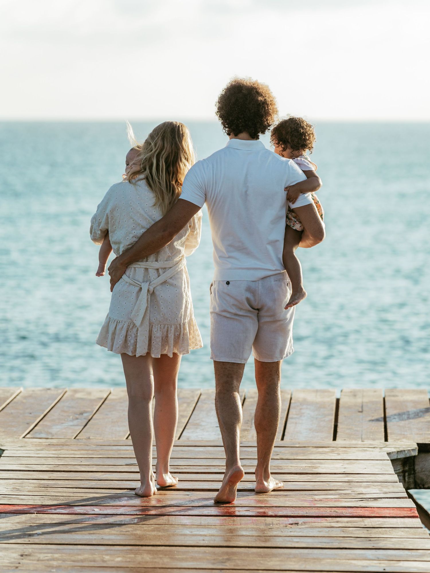 Family of four standing on a wooden pier gazing at the calm ocean horizon.