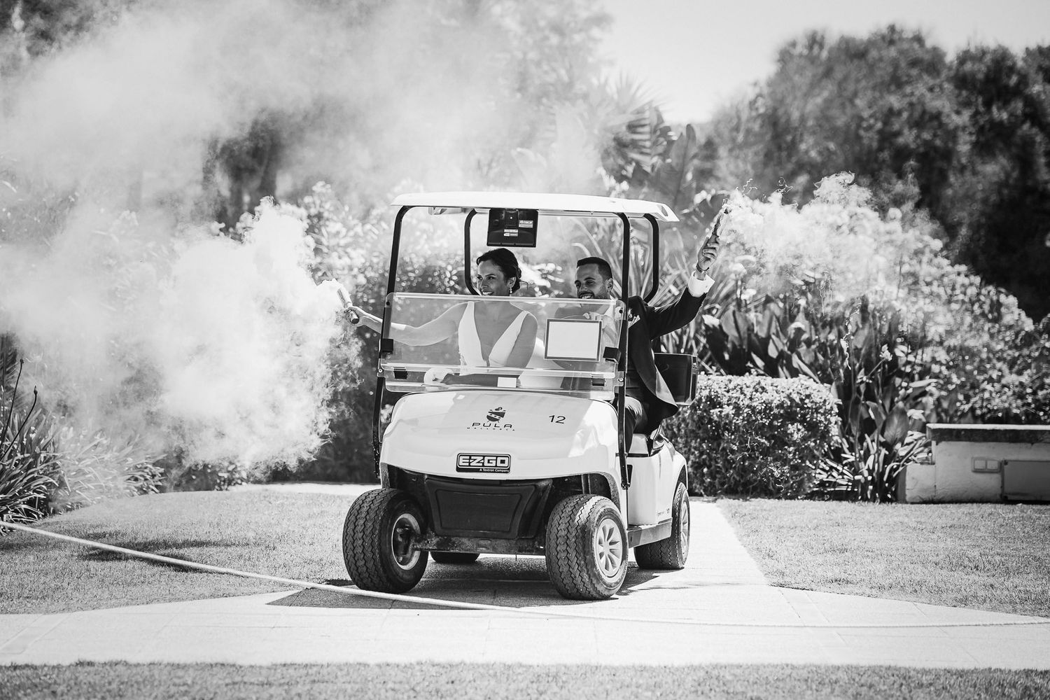 Black and white photo of wedding couple arriving in a golf cart surrounded by smoke effects.