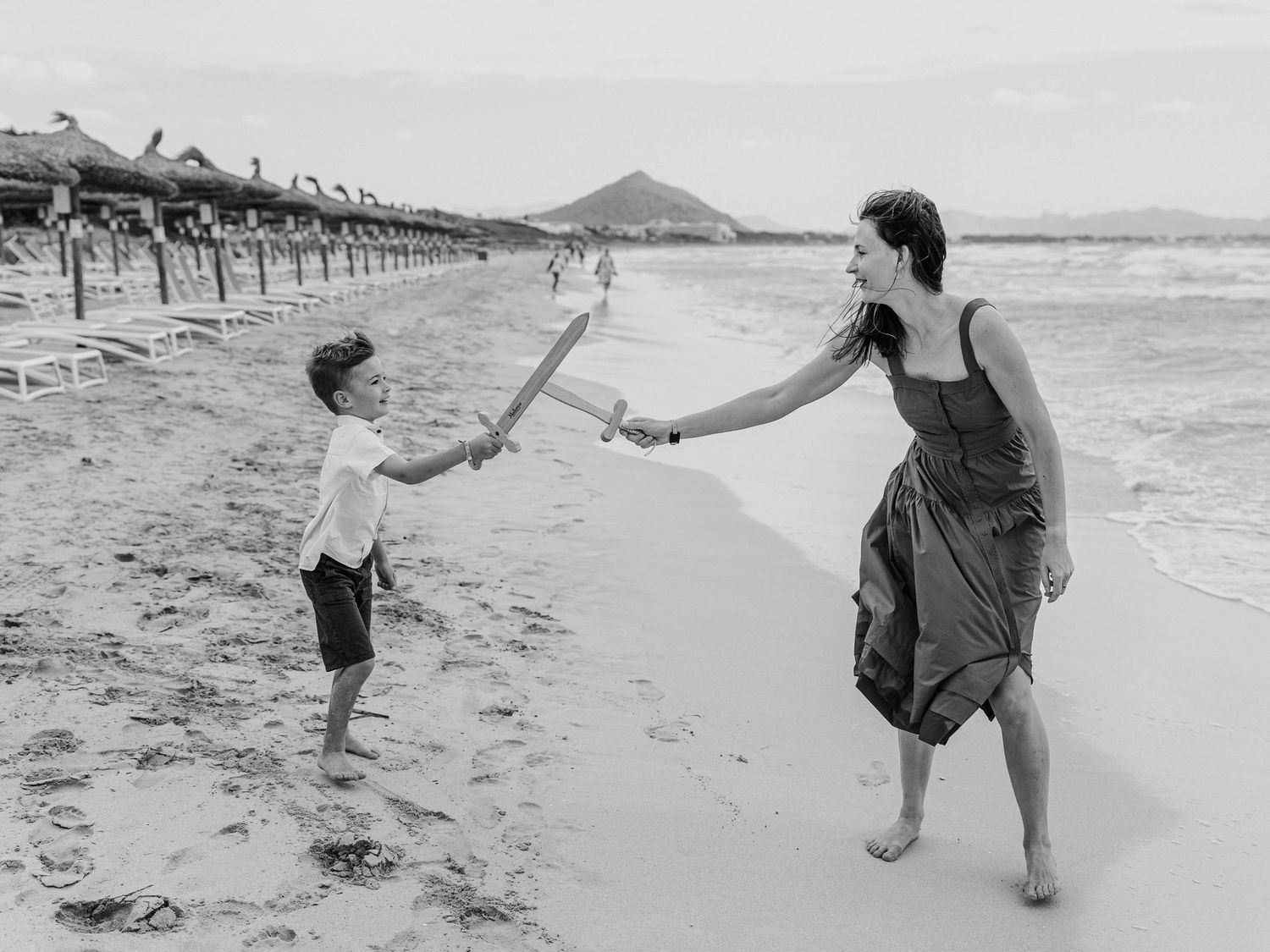 Black and white photo of mother and son playing with stick on beach.