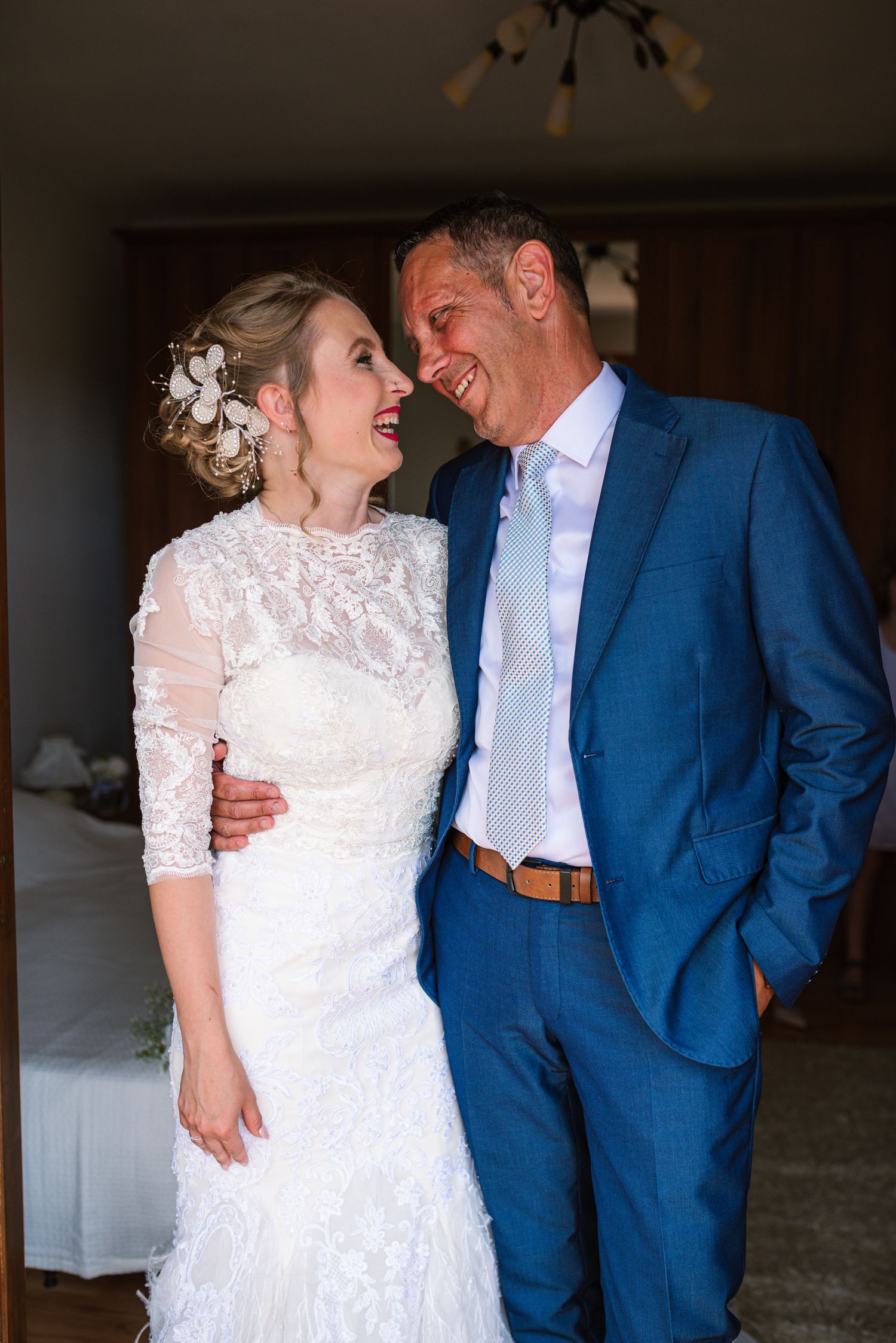 Laughing bride and groom in lace dress and blue suit sharing a joyful moment.