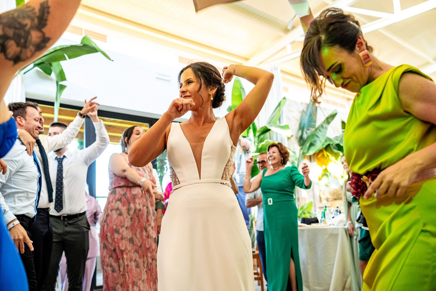 Bride in white gown dances energetically with guests at a vibrant outdoor wedding reception.