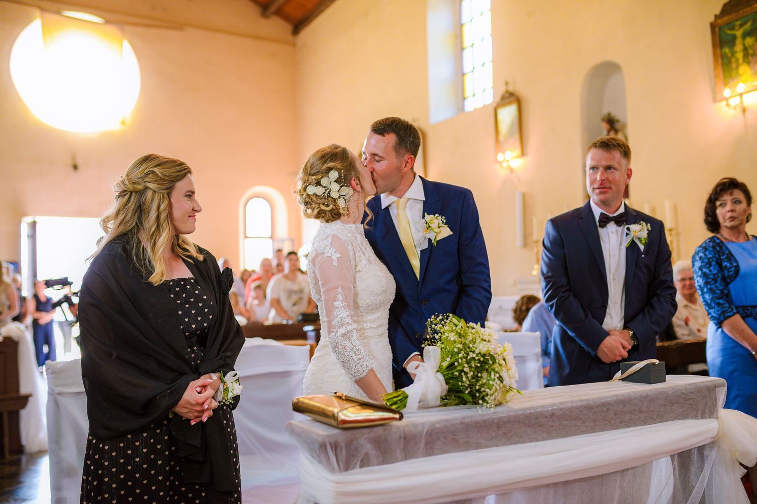 Bride and groom kiss at the altar during their wedding ceremony inside a warm church.