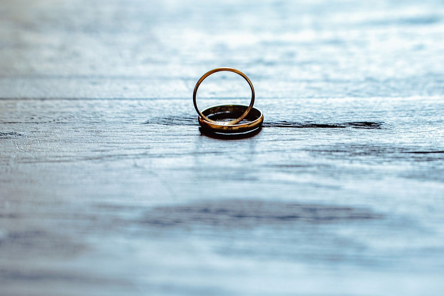 Two gold wedding bands resting together on a blue textured surface.