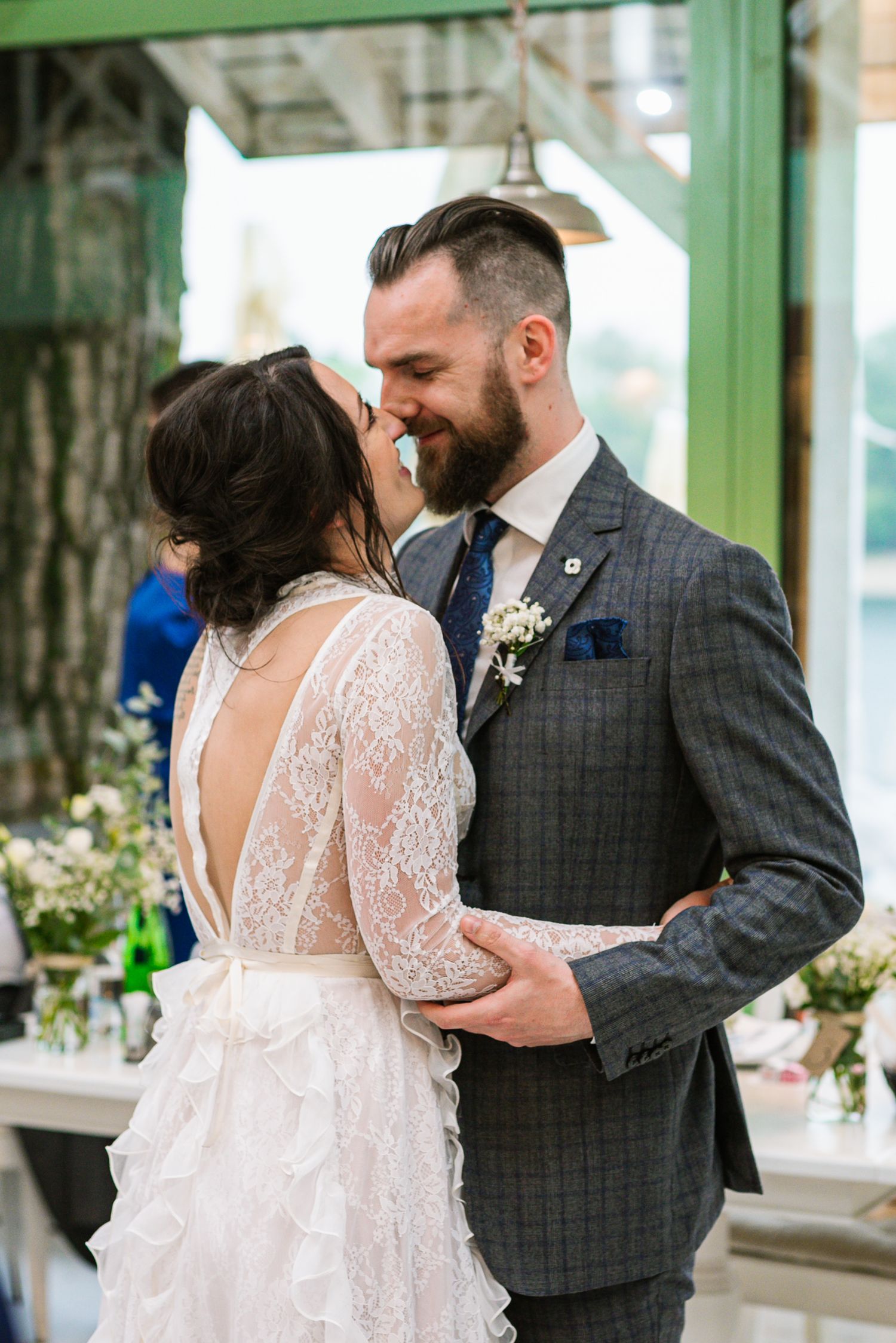 Bride and groom share a romantic first kiss in a lace backless wedding dress and gray plaid suit.