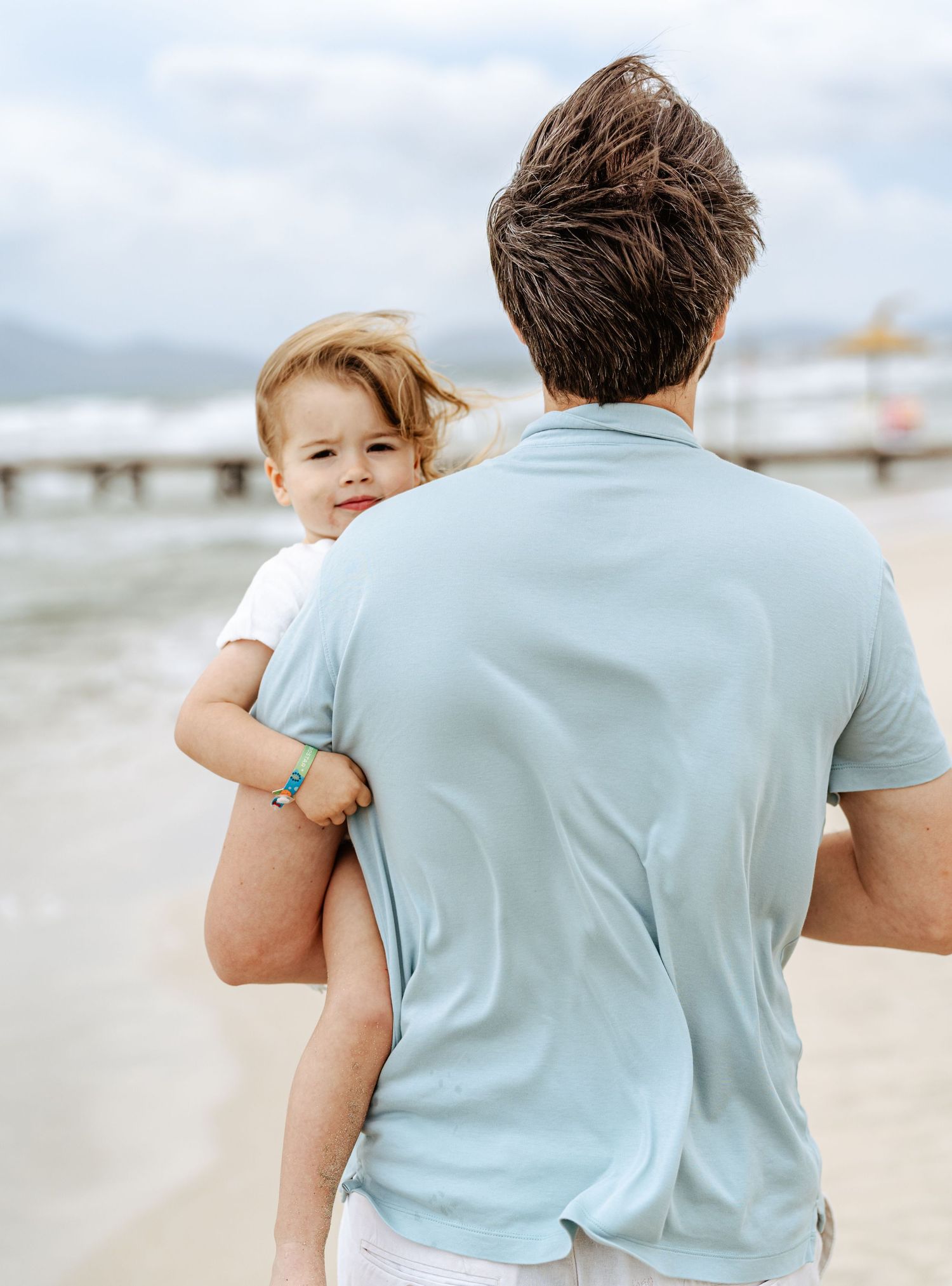 Father carrying toddler on shoulder walking along scenic beach pier.
