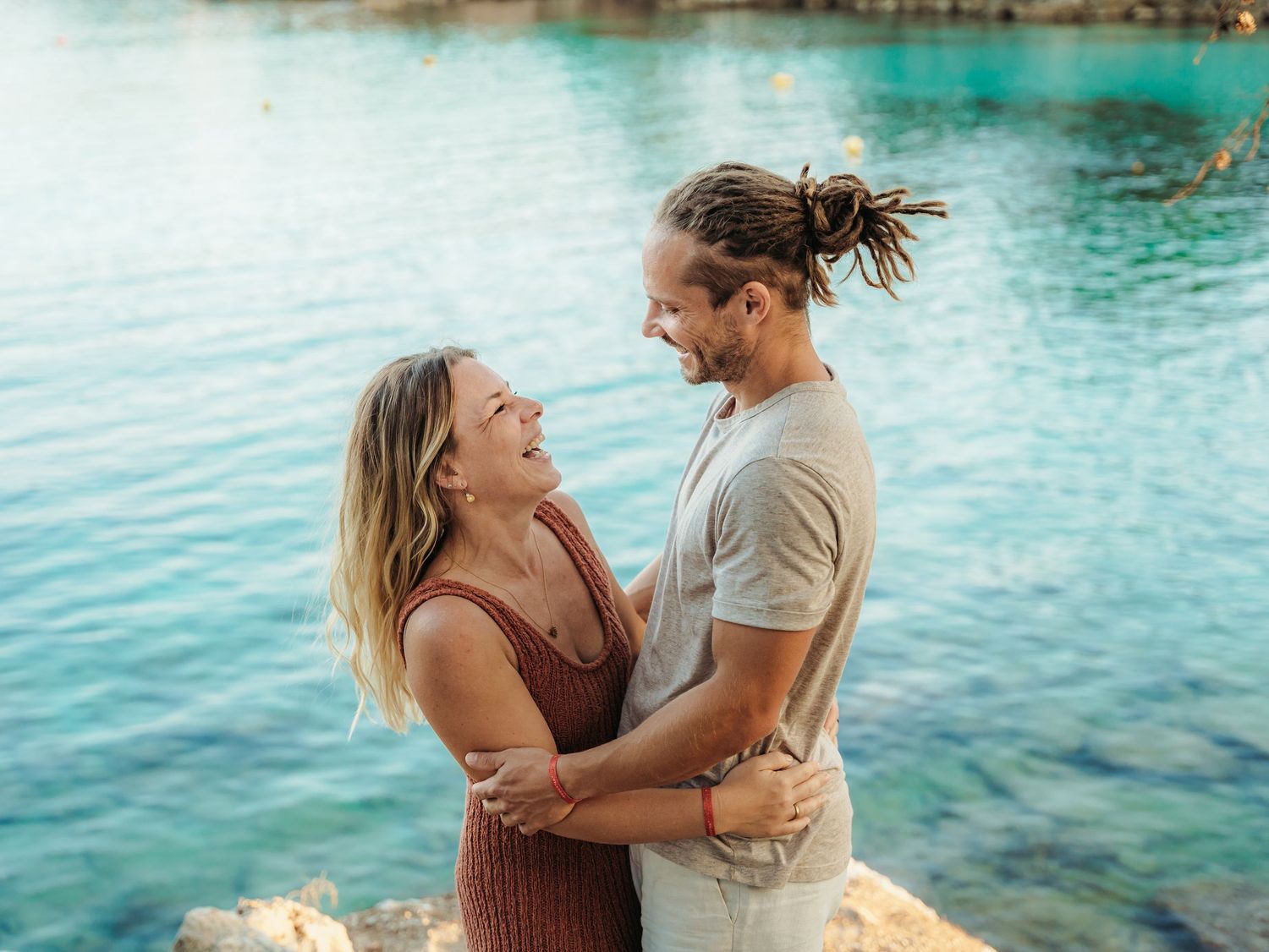 Smiling couple holding each other and gazing lovingly by bright turquoise coastal water.
