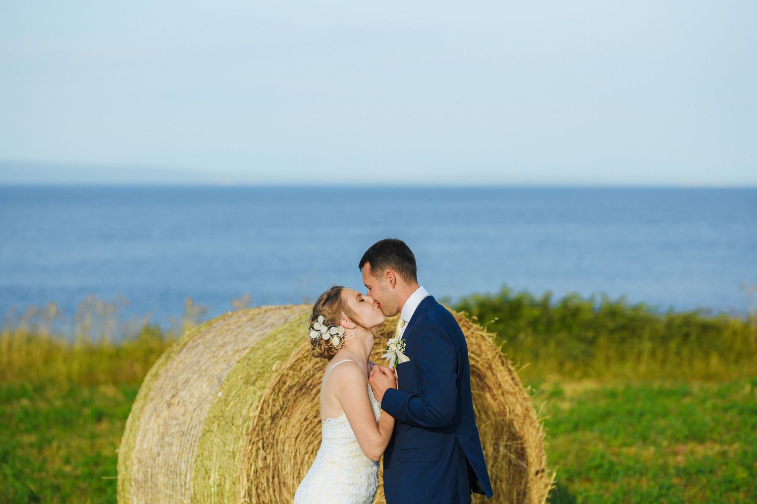 Bride and groom sharing a kiss between fields and sea - a quiet promise held in the landscape. Herzenshaus Studio, Frankfurt.