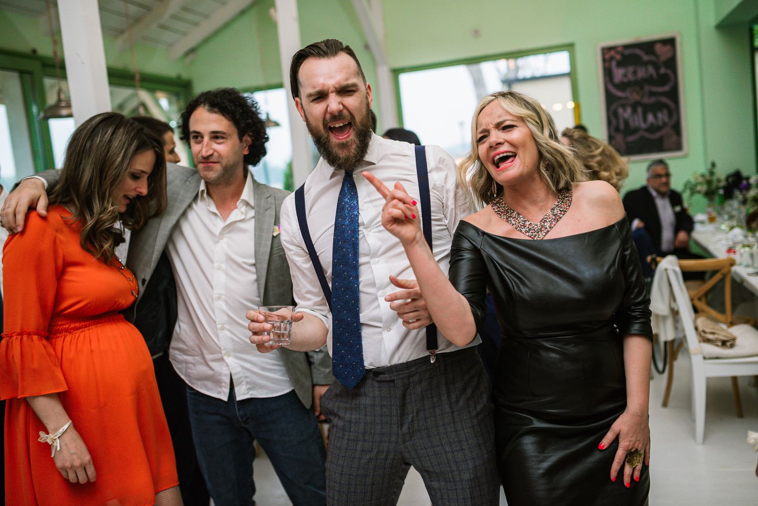 Excited wedding guests laughing and celebrating together at a festive indoor reception.