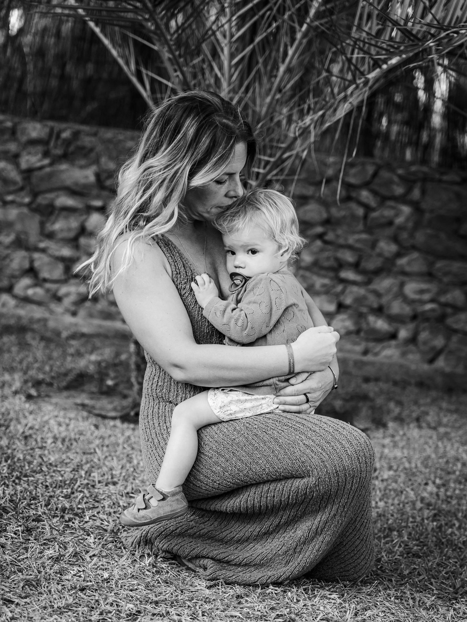 Black and white portrait of loving mother cuddling baby boy on grass outdoors.