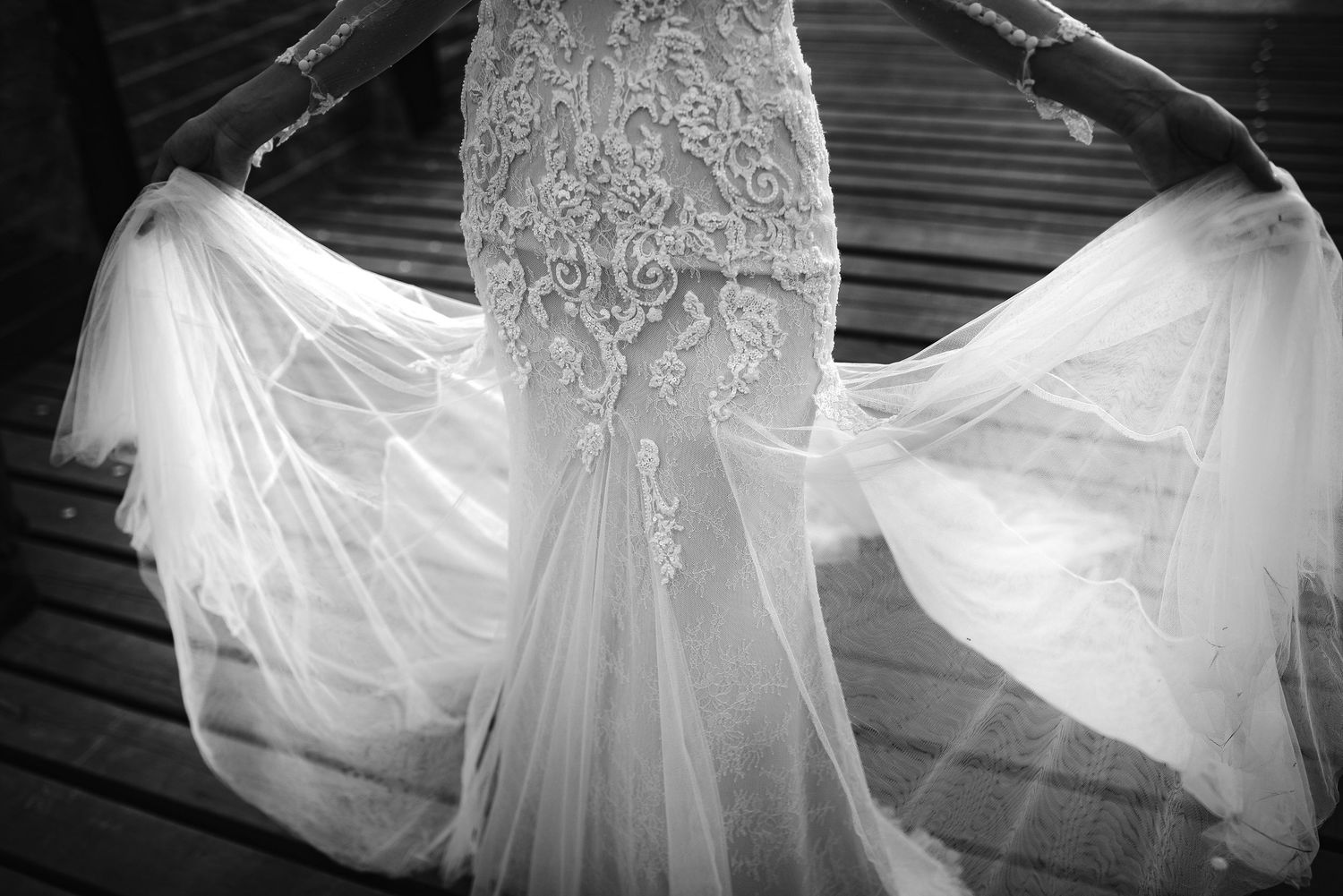 Close-up black and white detail of intricate lace embroidery on a flowing bridal gown.