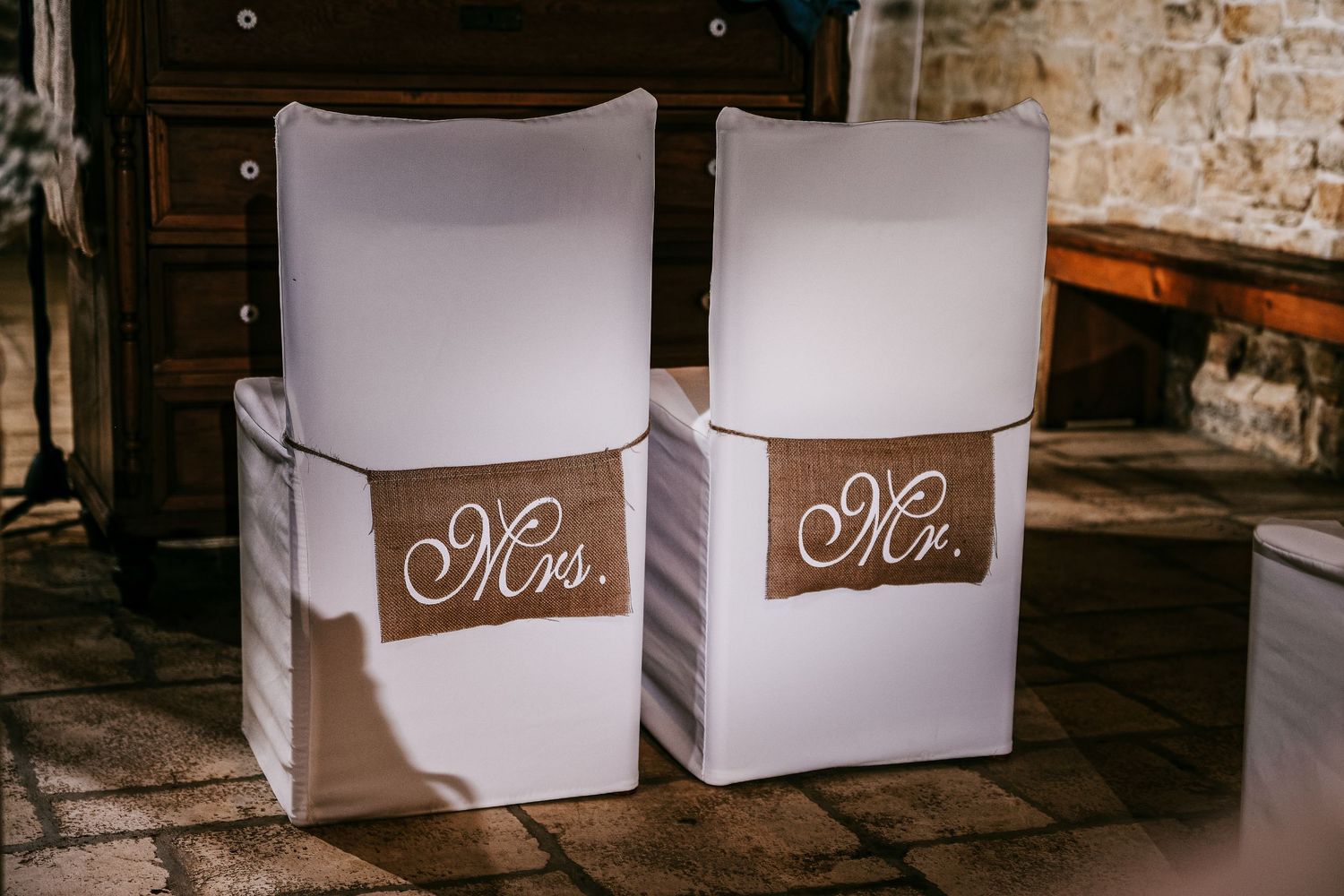 White wedding chairs decorated with burlap Mrs. and Mr. signs for the bride and groom.