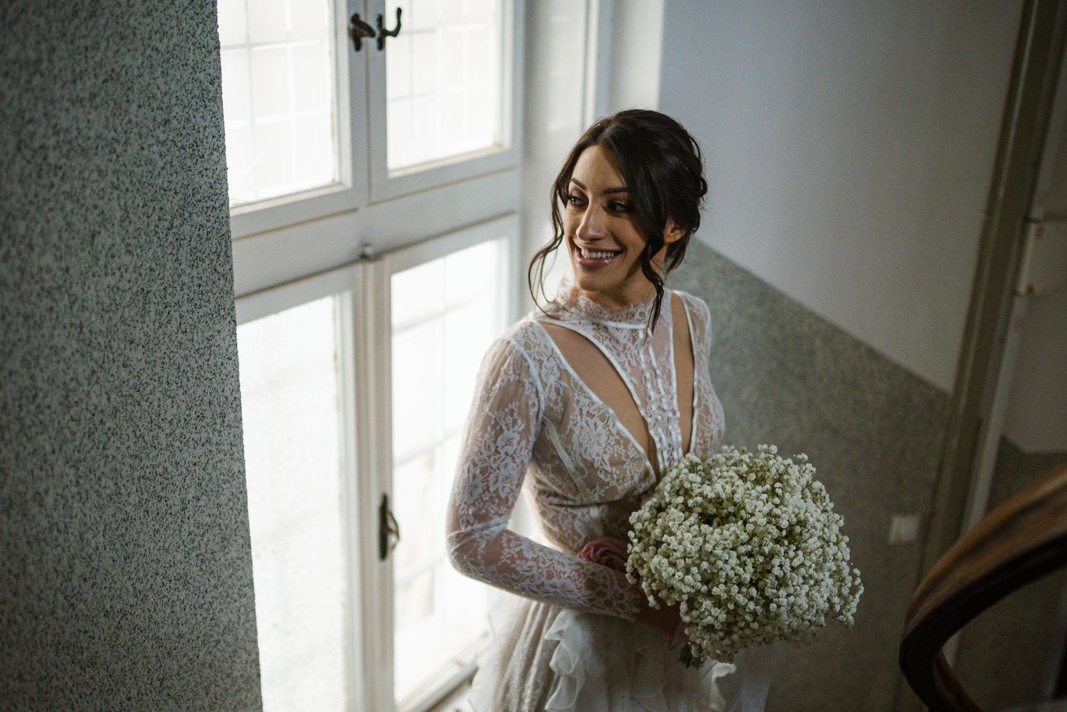 Radiant bride in lace gown laughing while holding white baby's breath bouquet.