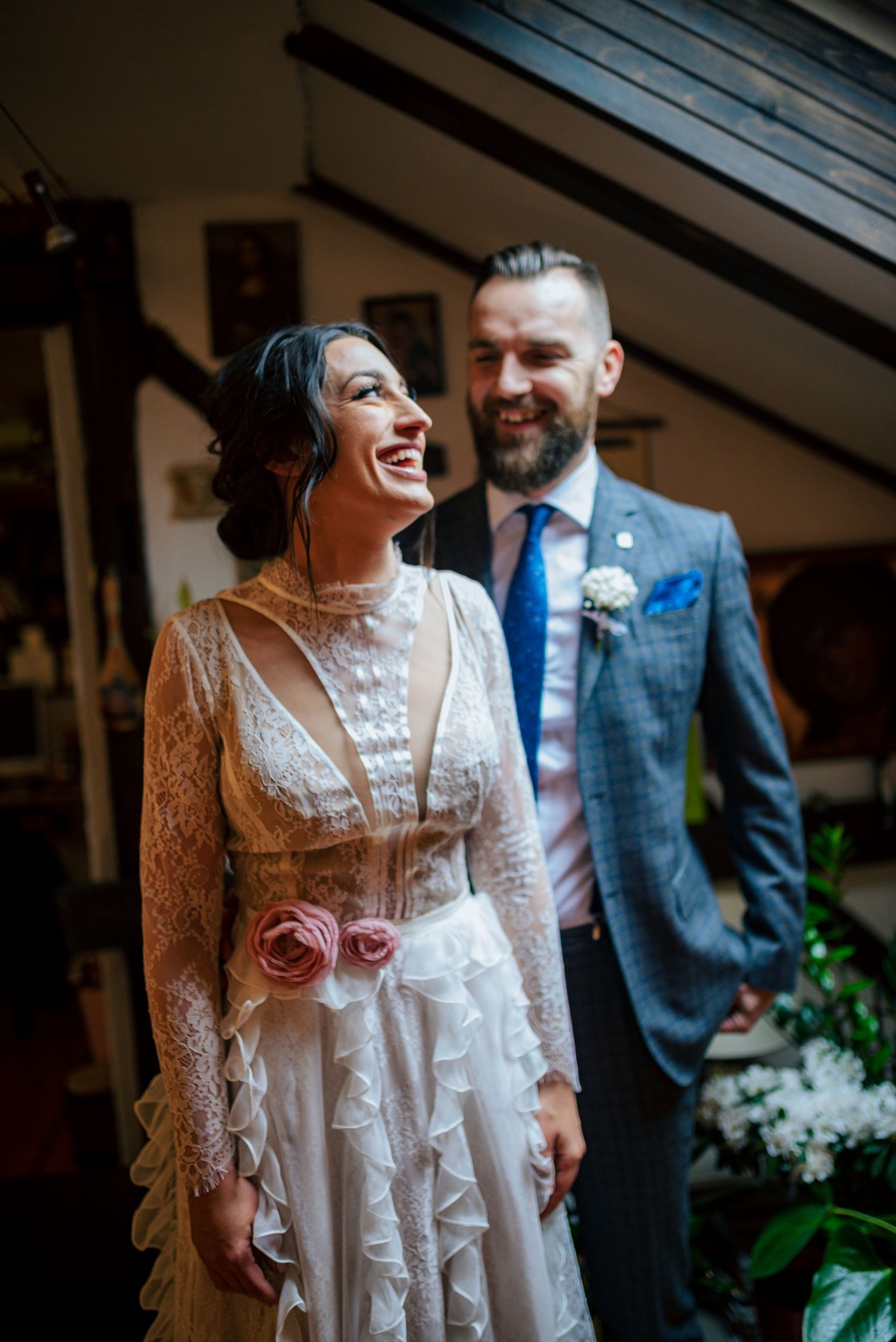 Laughing bride in vintage lace dress with groom in blue suit at wedding.