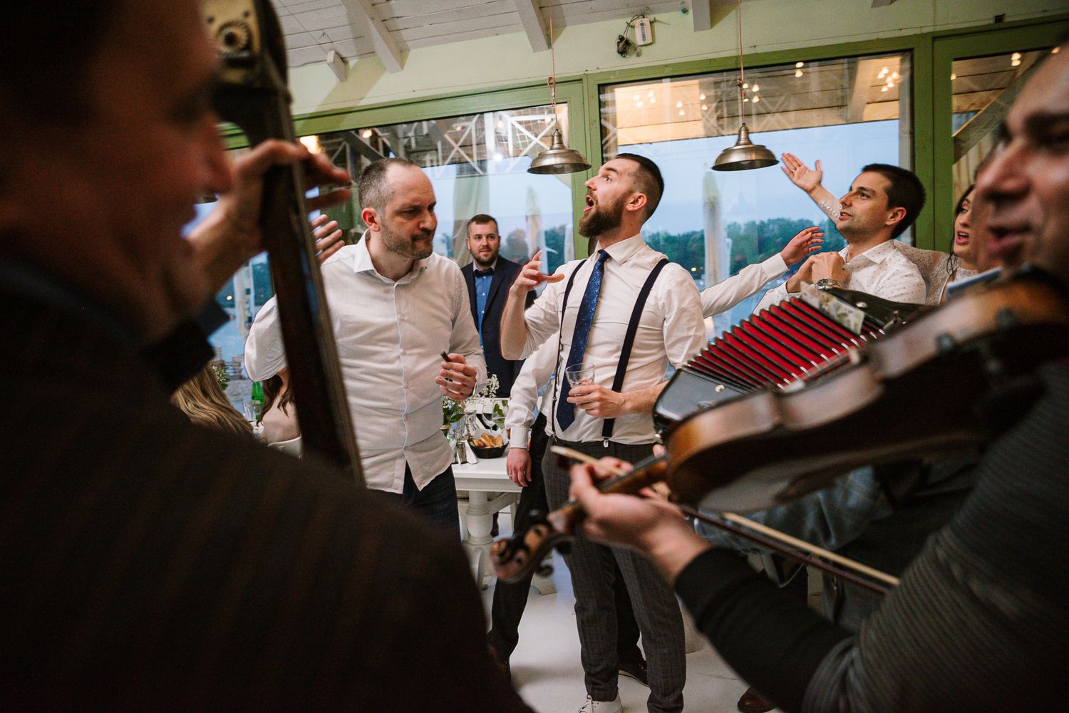 Groom sings joyfully with live band musicians playing accordion and strings at wedding.