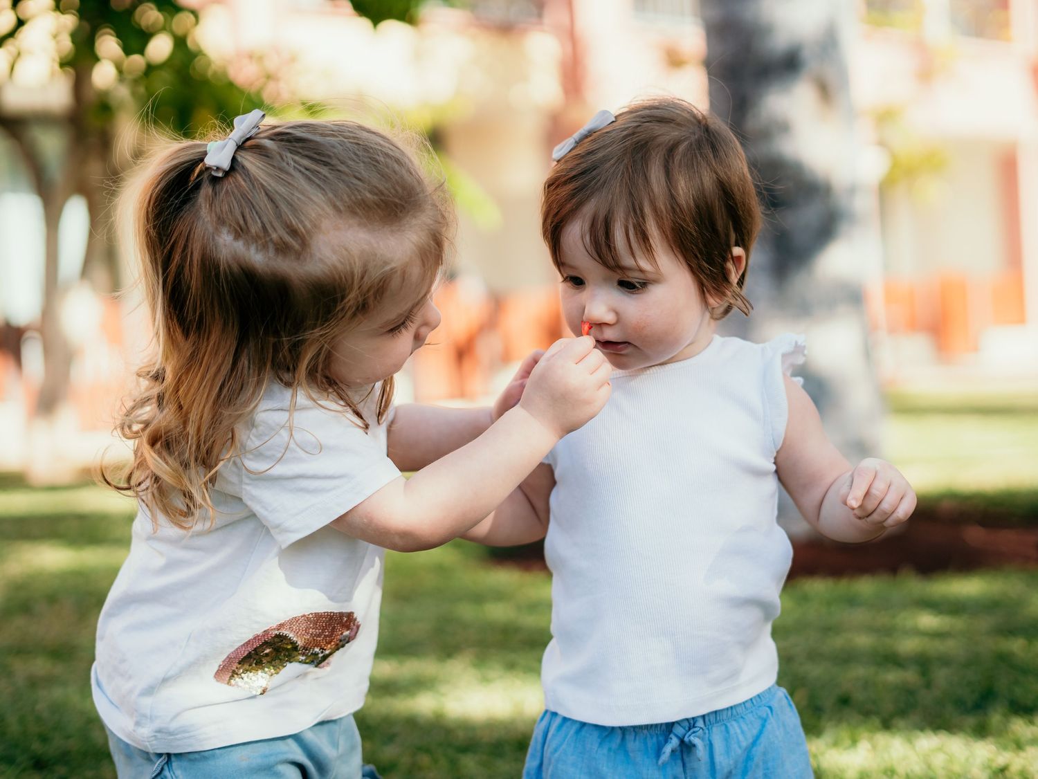 Two young sisters sharing a tender moment outdoors, natural family photography capturing childhood connection and affection.