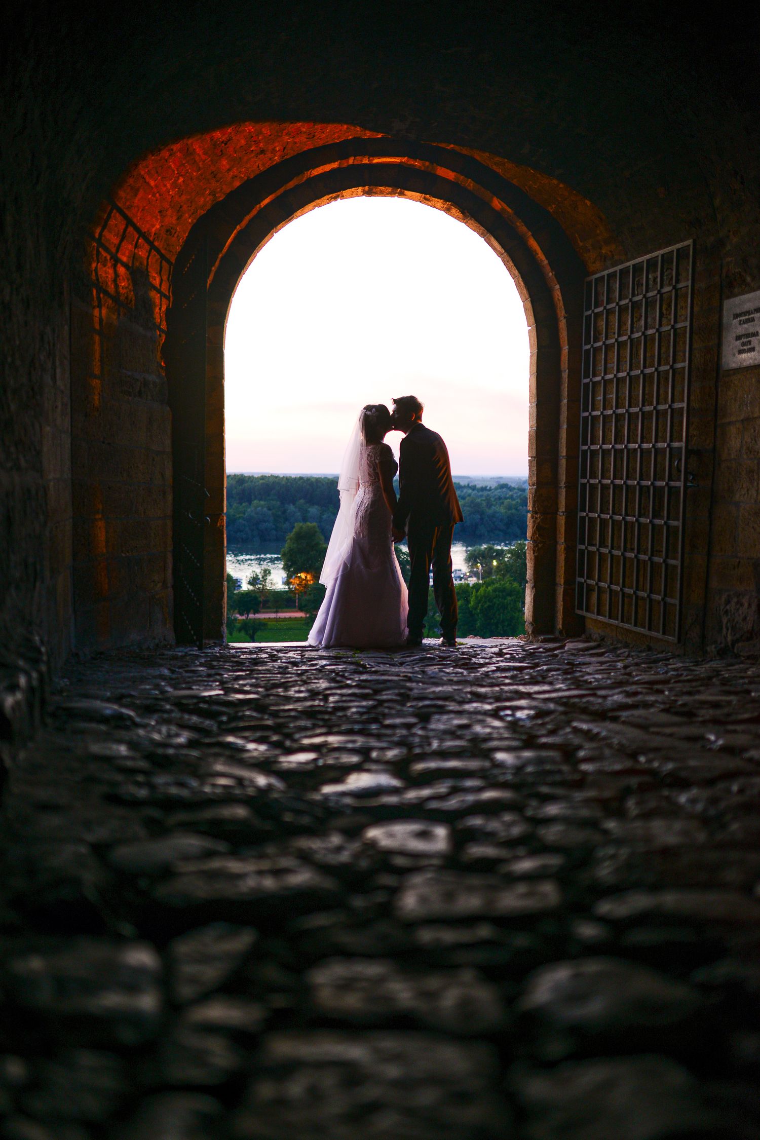 Silhouette of bride and groom kissing in a stone archway at sunset on their wedding day.