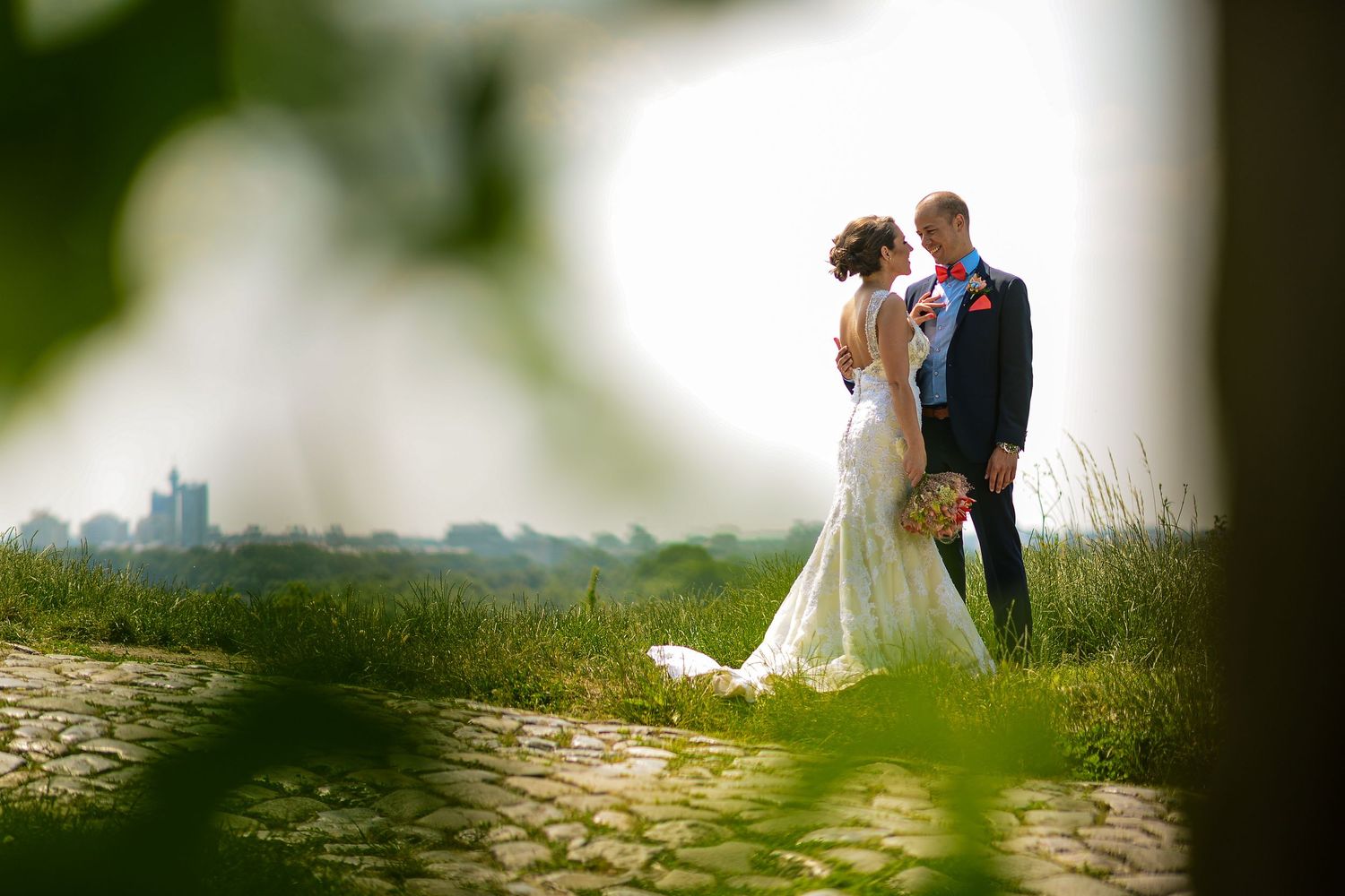 Bride and groom stand together on a scenic hilltop with a countryside backdrop on their wedding day.