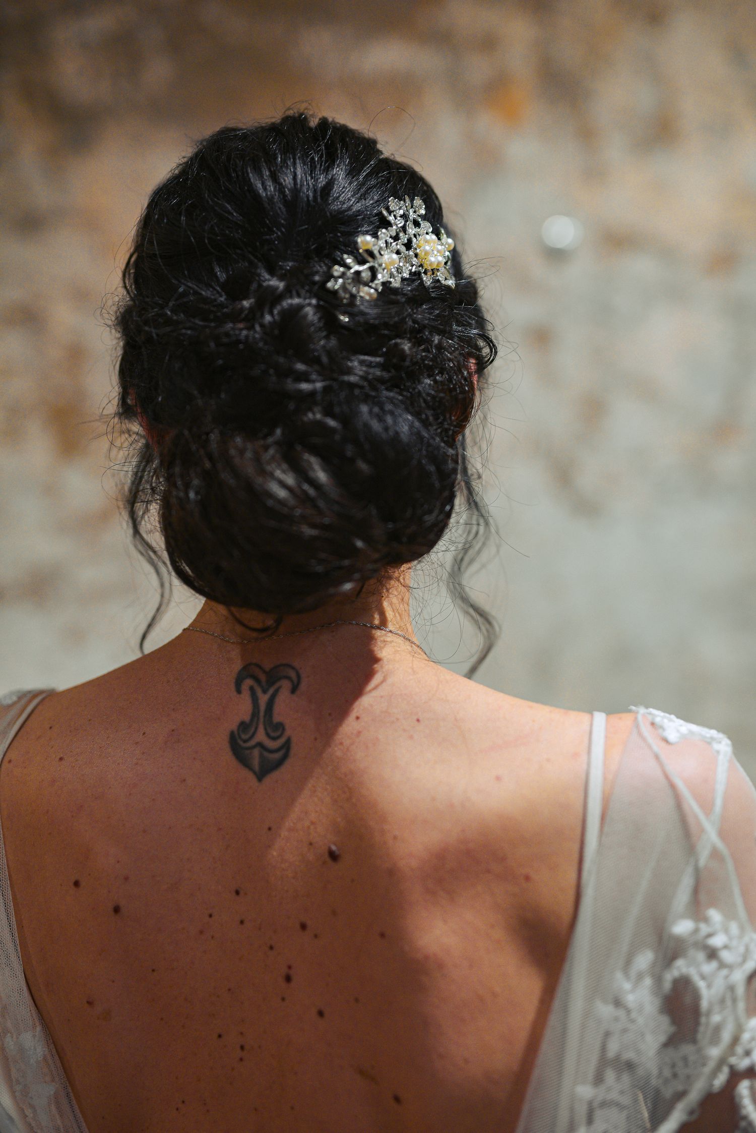 Back view of bride with elegant updo, floral hair comb, and neck tattoo.