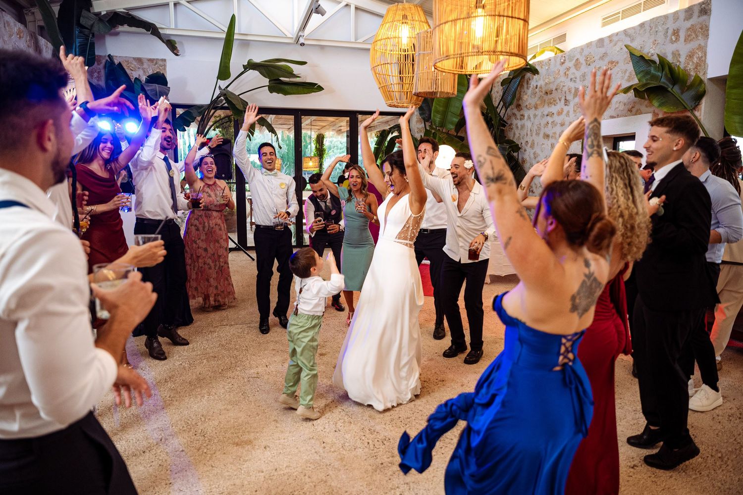 Bride in white gown walks through a celebratory tunnel of cheering wedding guests on the dance floor.