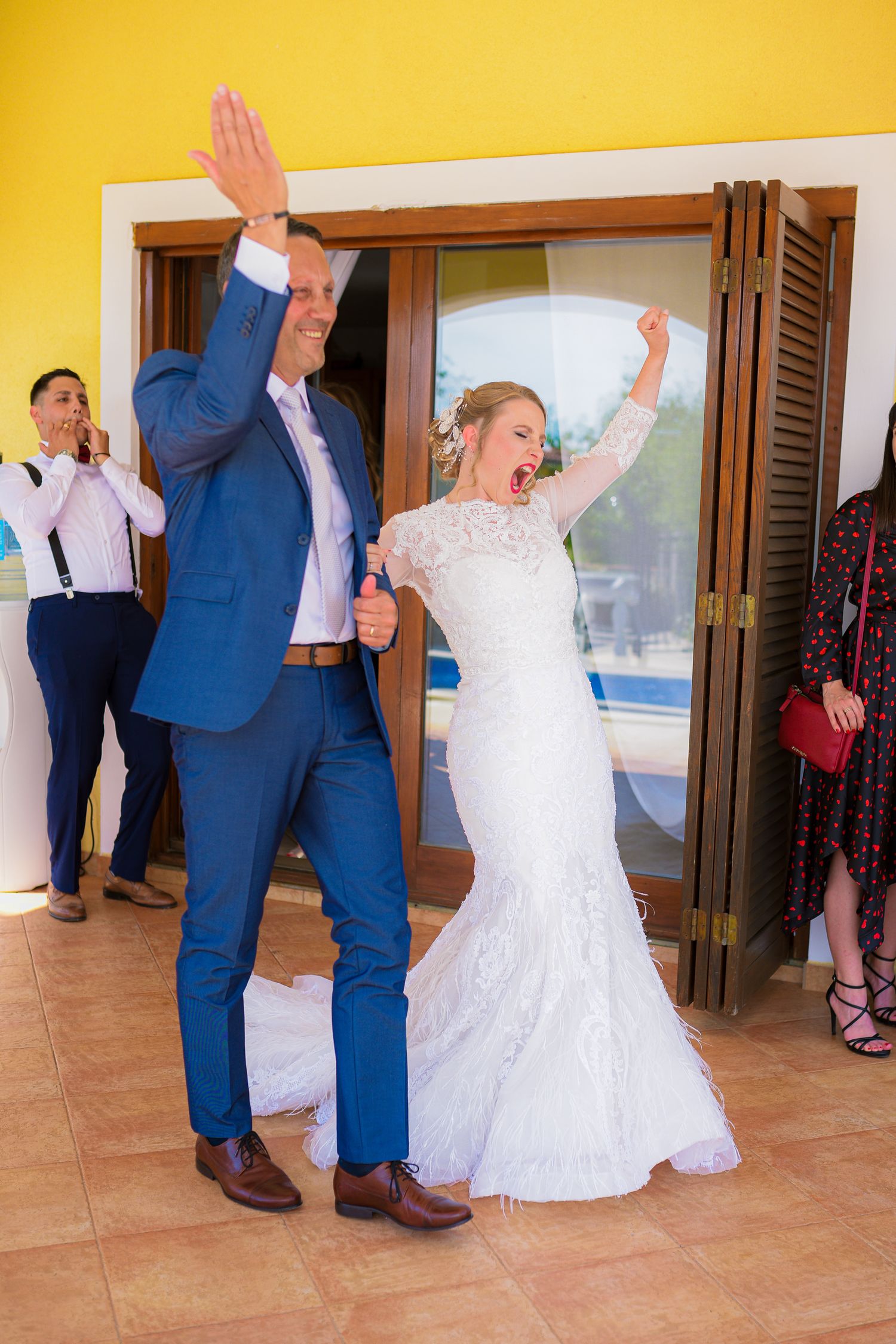 Excited bride and groom raising arms triumphantly while making grand entrance at wedding reception.