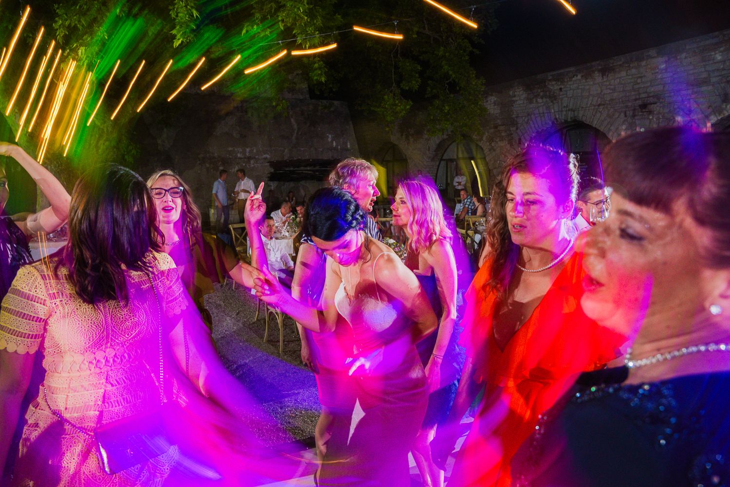 Wedding guests dancing energetically under colorful neon lights at night reception.