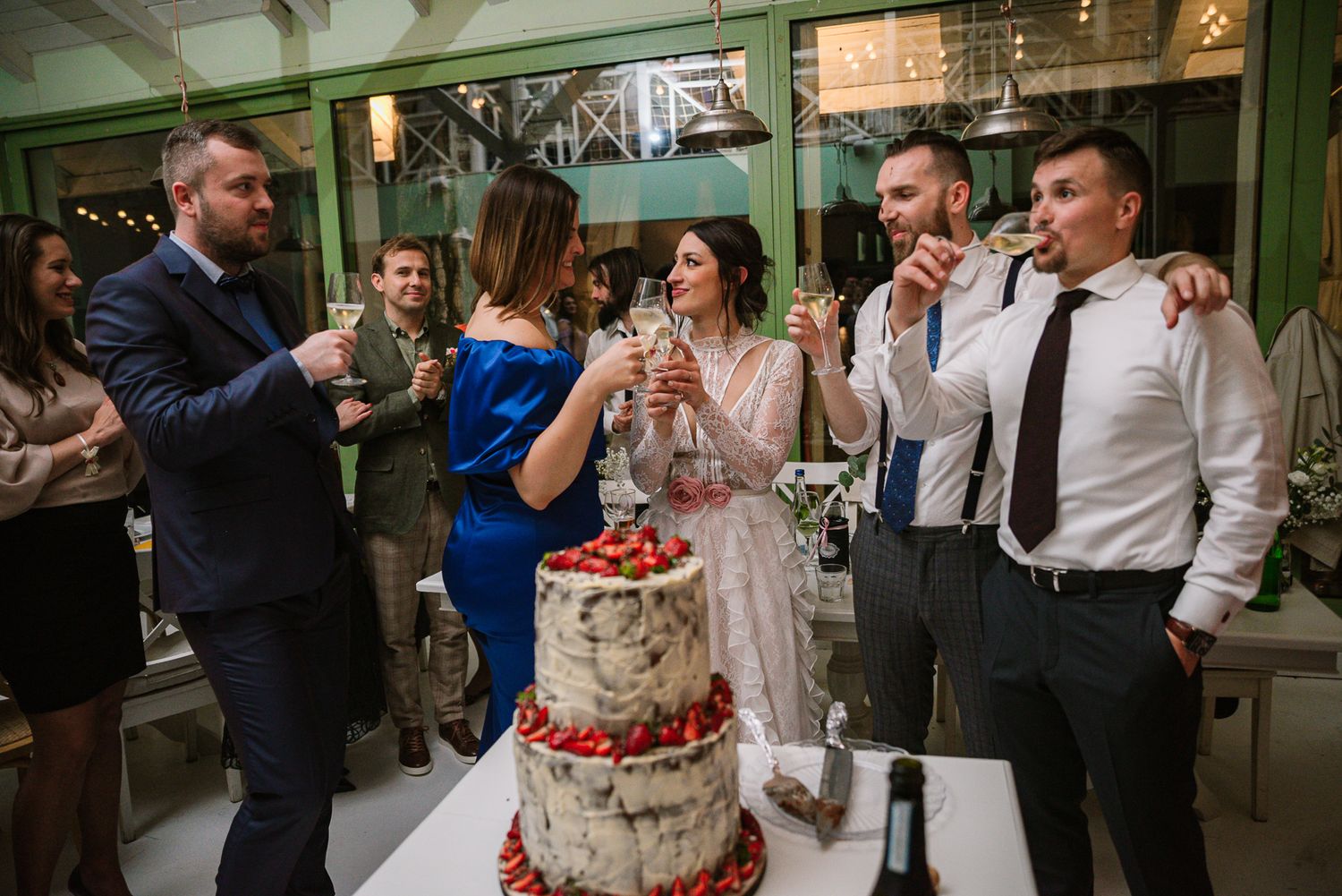 Wedding party toasts with champagne beside a rustic strawberry naked wedding cake.