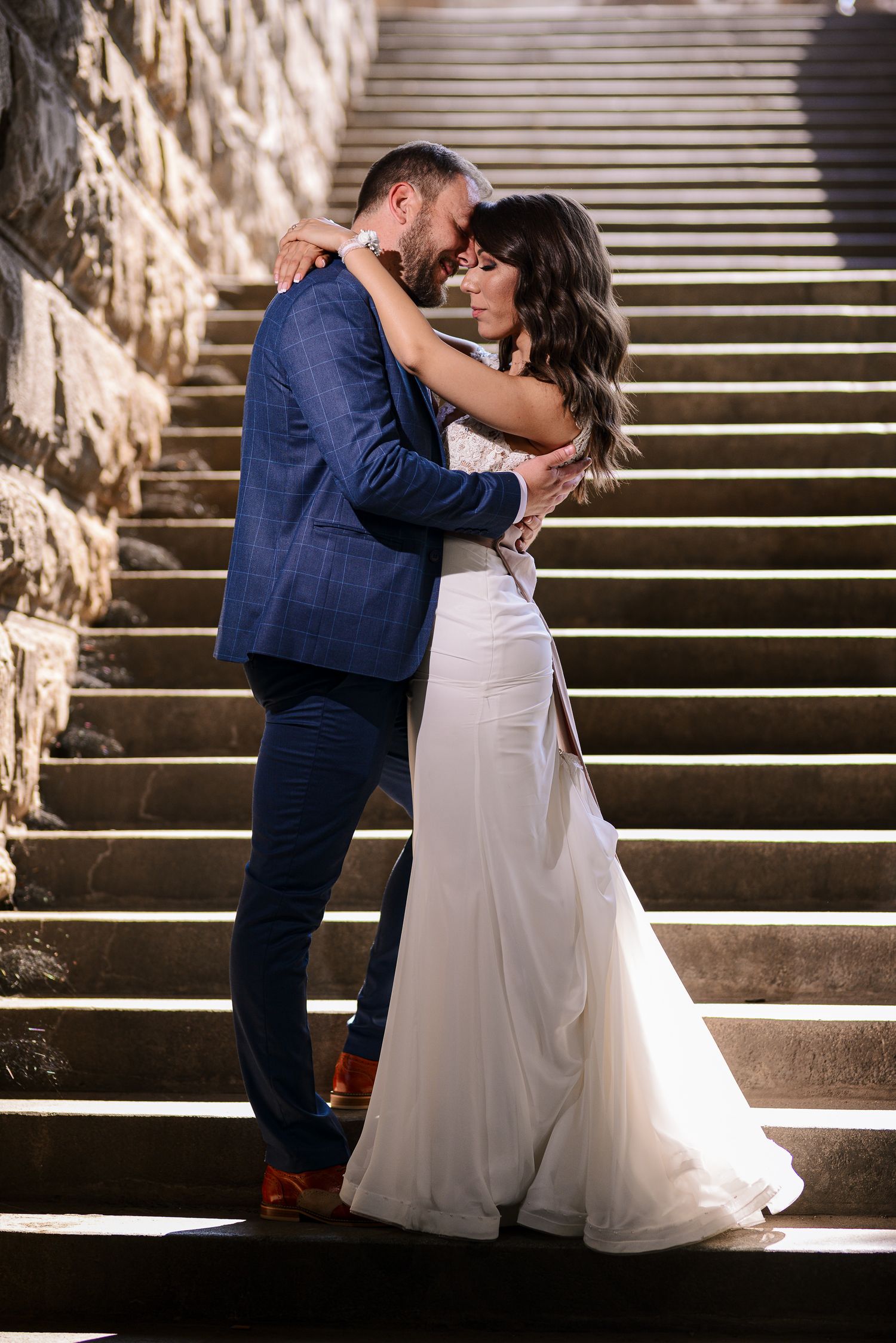 Bride and groom embrace romantically on dramatic stone steps in a stunning evening wedding portrait.
