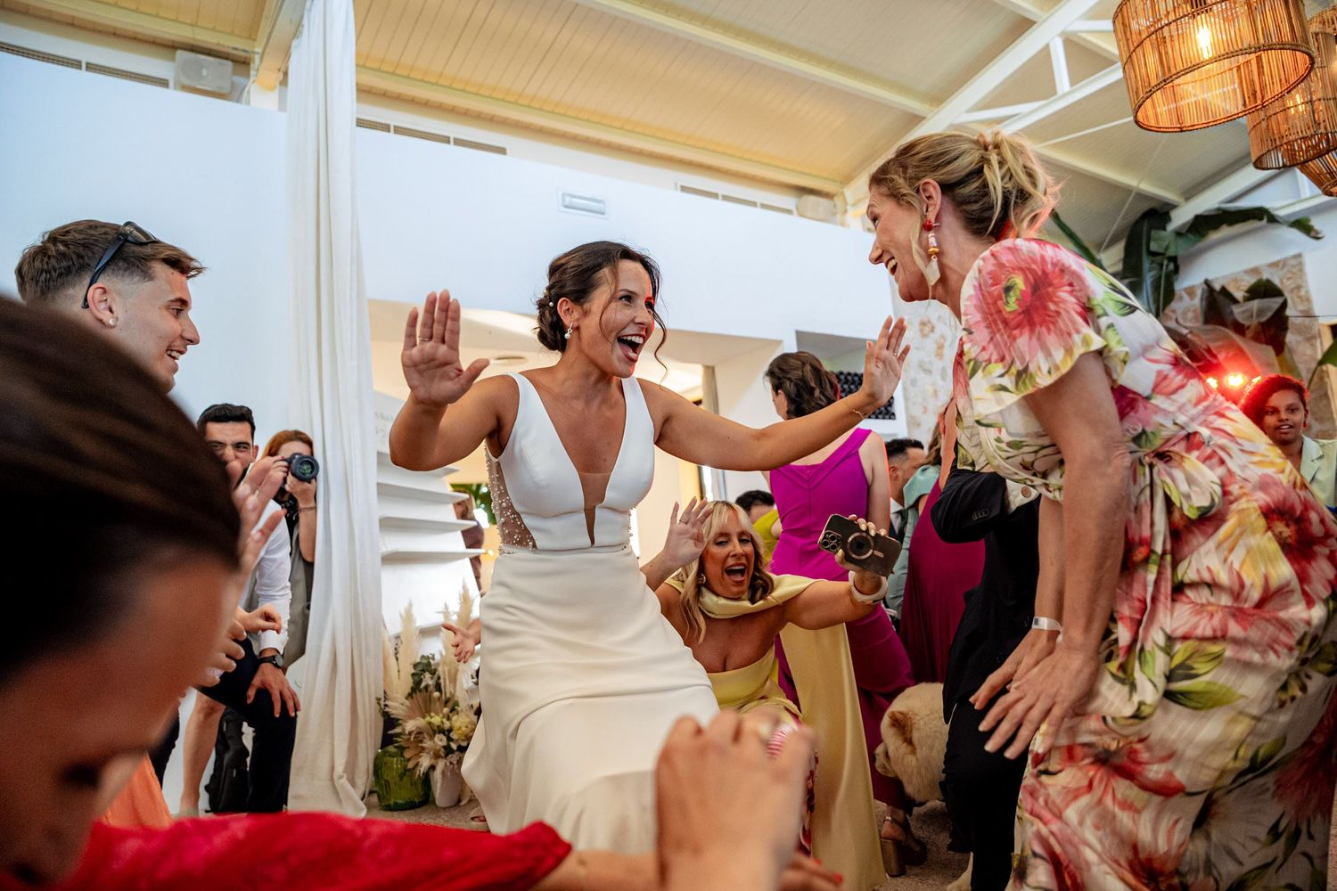 Bride in white dress laughs and high-fives guests during a joyful wedding celebration.