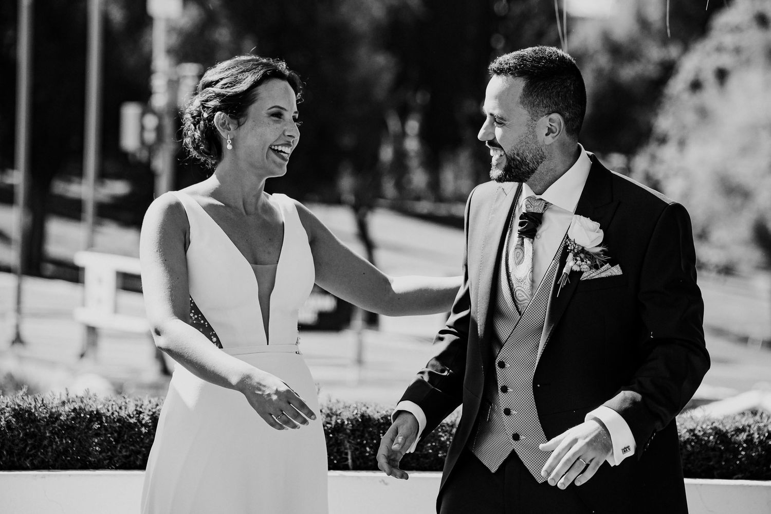 Bride and groom share a joyful laugh together outdoors in a classic black and white wedding portrait.
