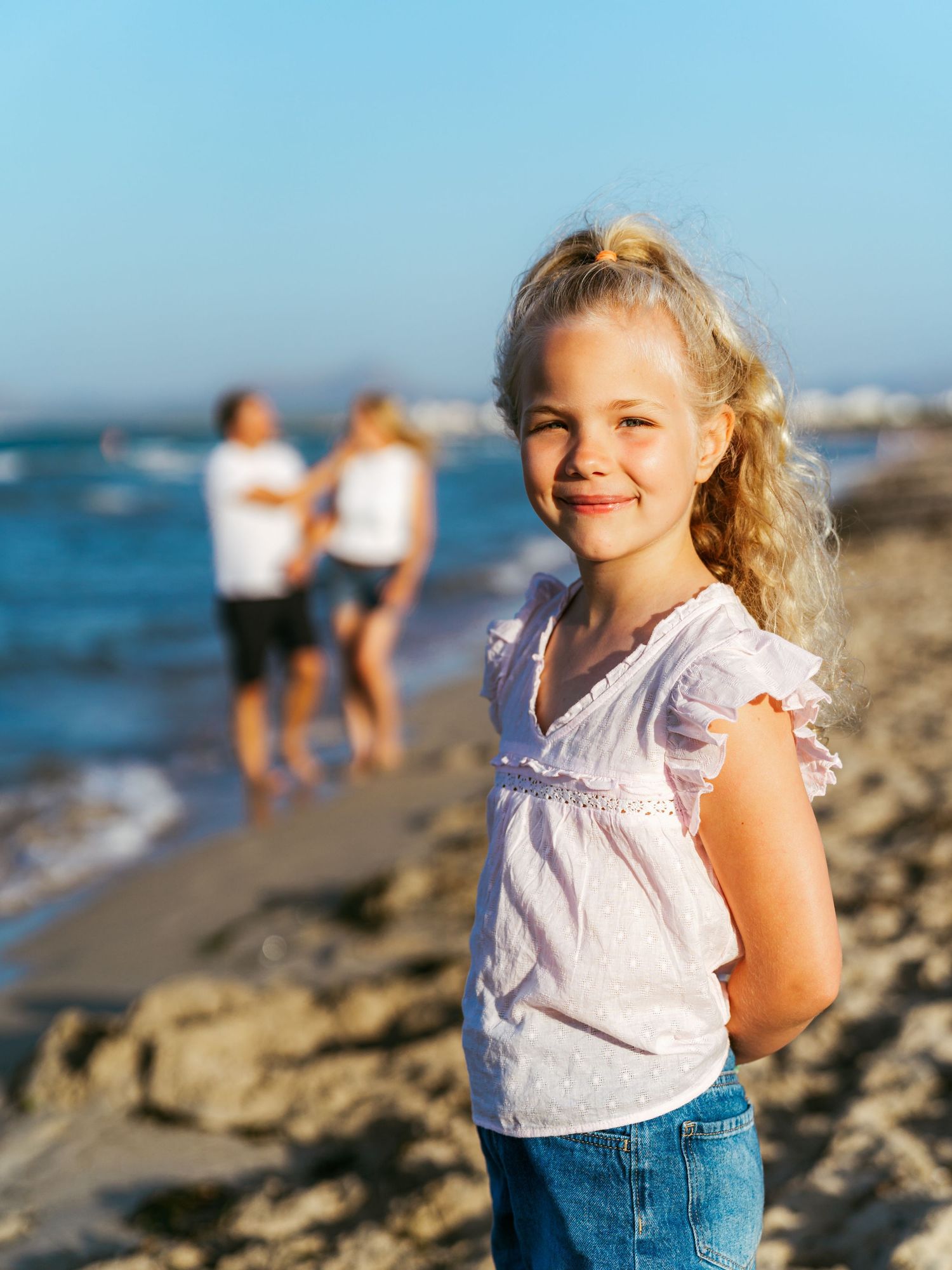 Young girl smiling on the beach with her family behind her, natural family photogrqphy by Herzenshaus Studio
