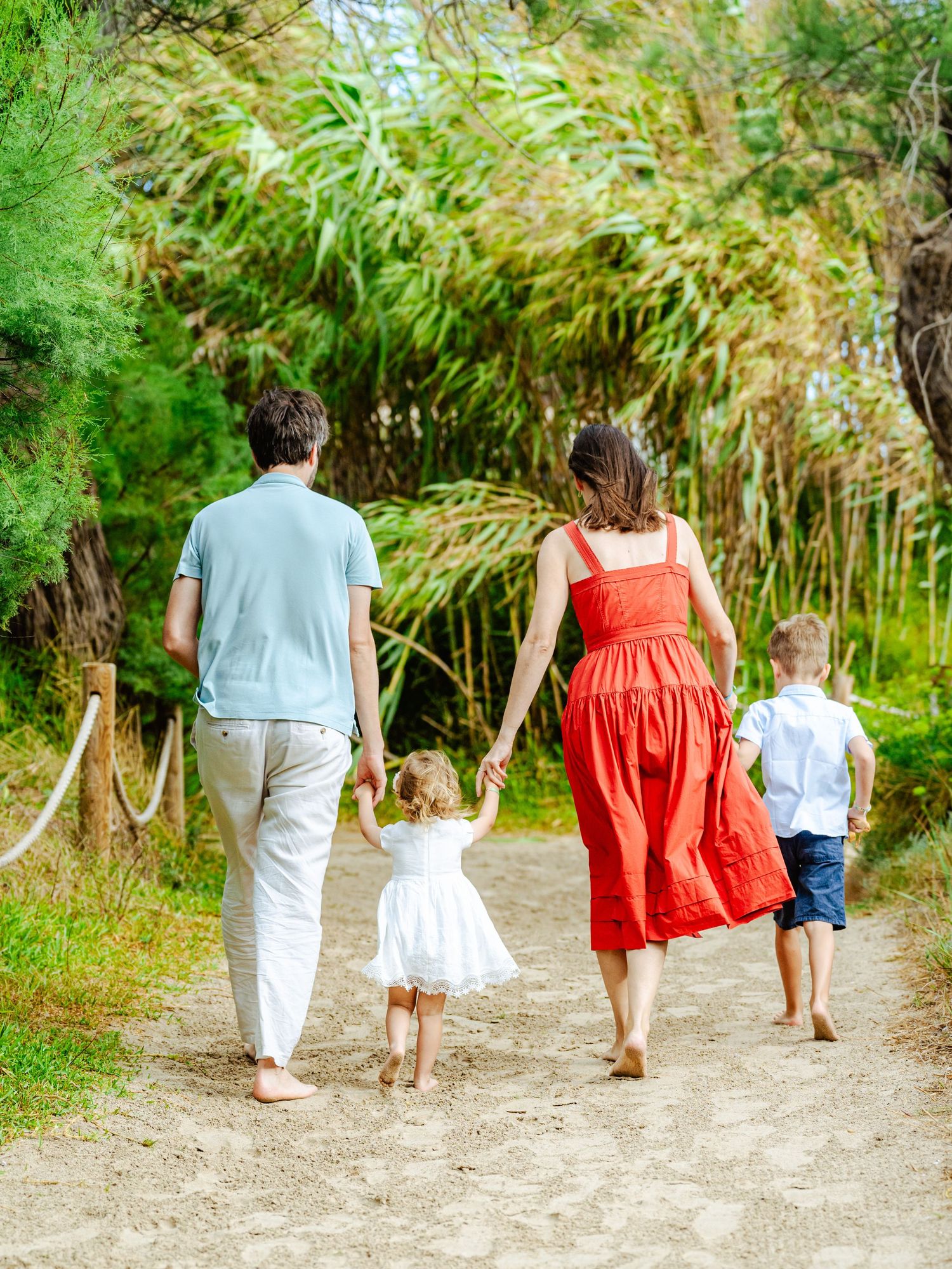 Family of four walking hand in hand down a sandy path surrounded by lush green trees and bamboo.