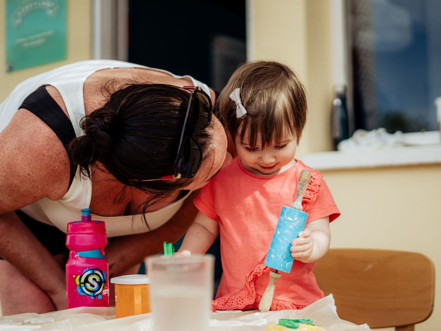 Mother and toddler daughter bonding over a dough activity at a colorful classroom table.