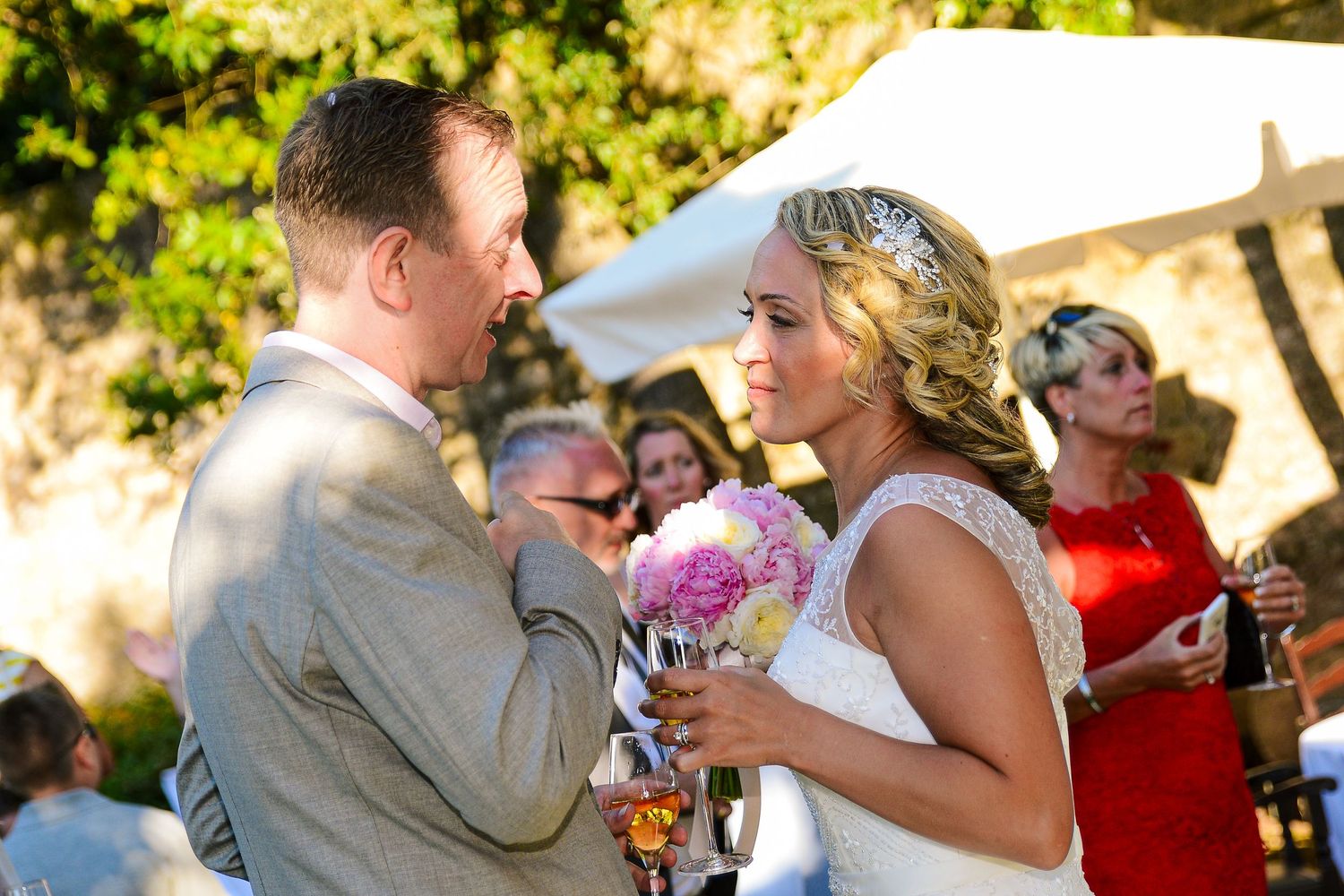 Bride holding pink bouquet exchanges loving glance with groom during outdoor wedding ceremony.