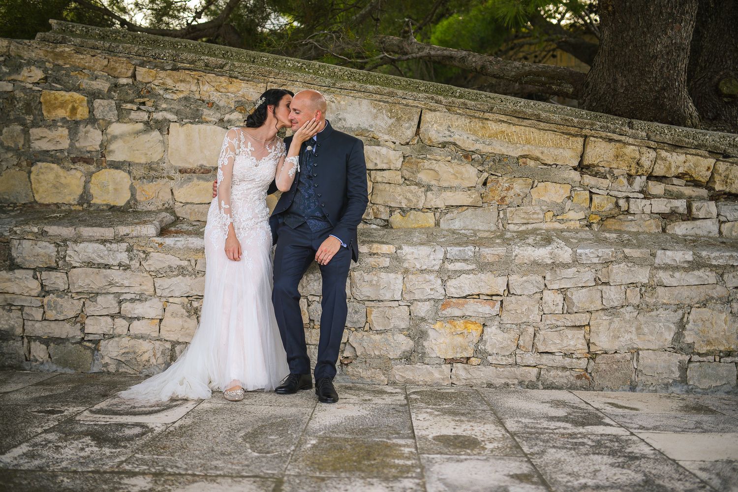 Wedding couple sharing a tender moment against a rustic stone wall outdoors.