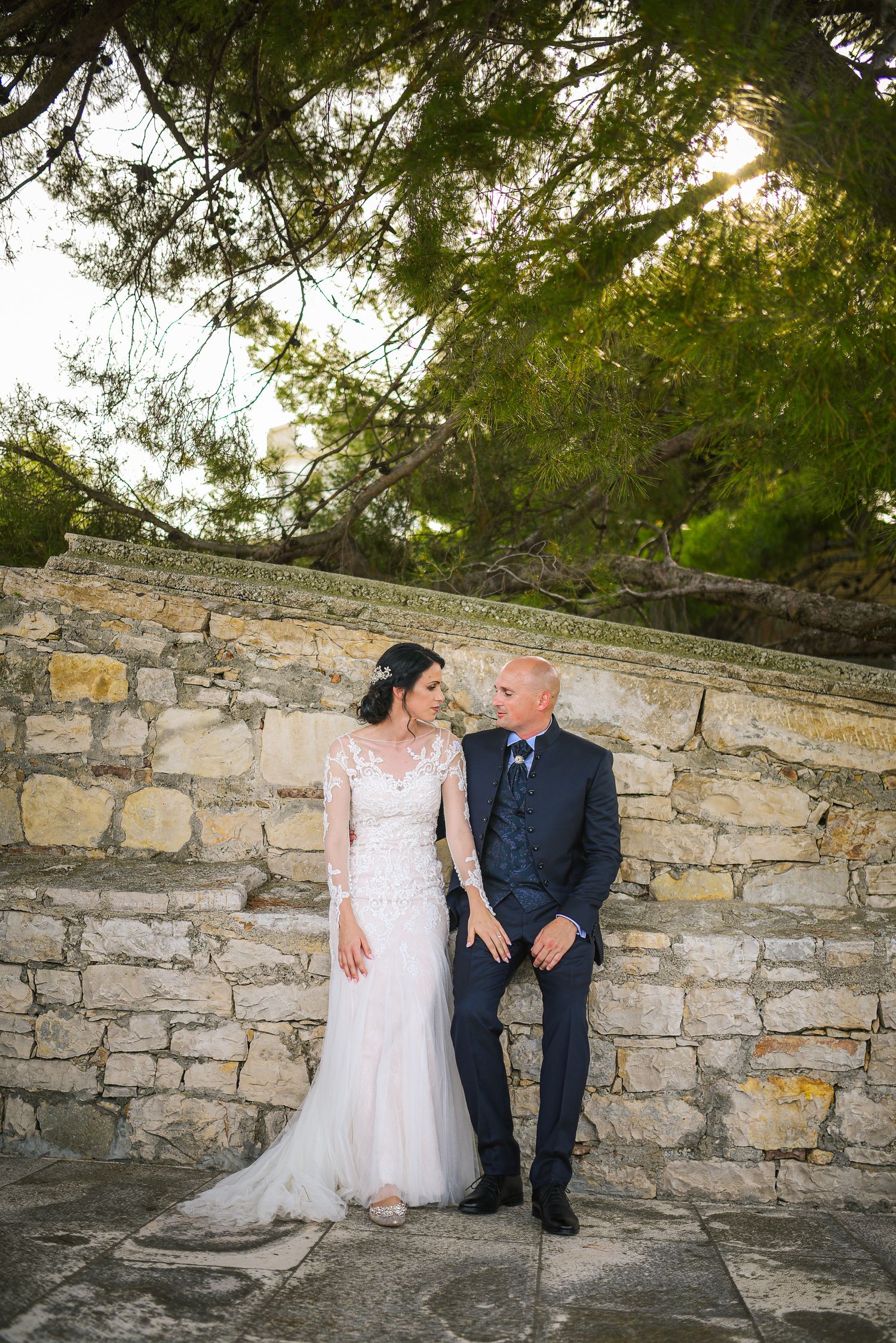 Bride and groom sharing a romantic moment against a rustic stone wall in an outdoor setting.