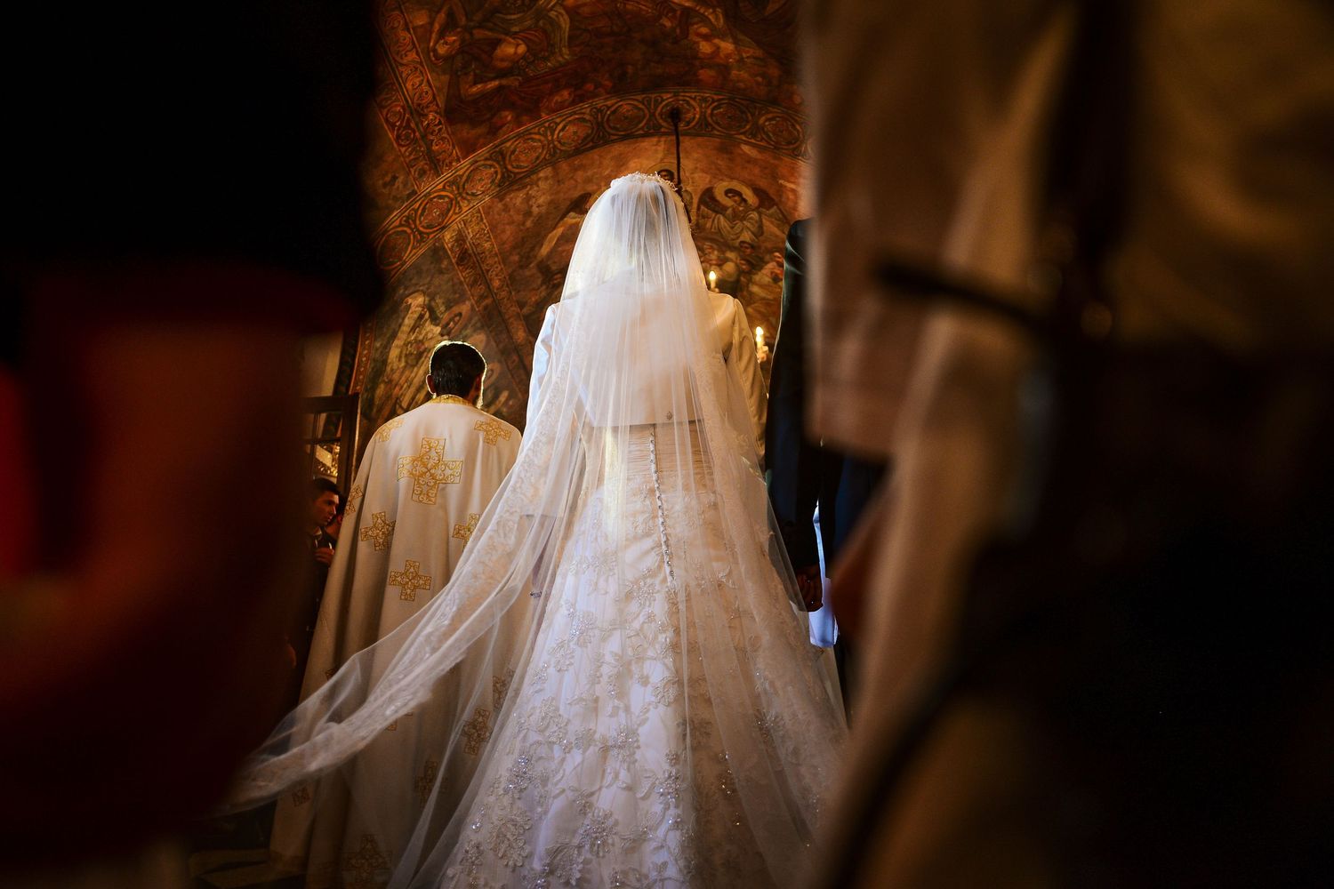 Bride in a long white veil walks through an ornate church during a traditional wedding ceremony.