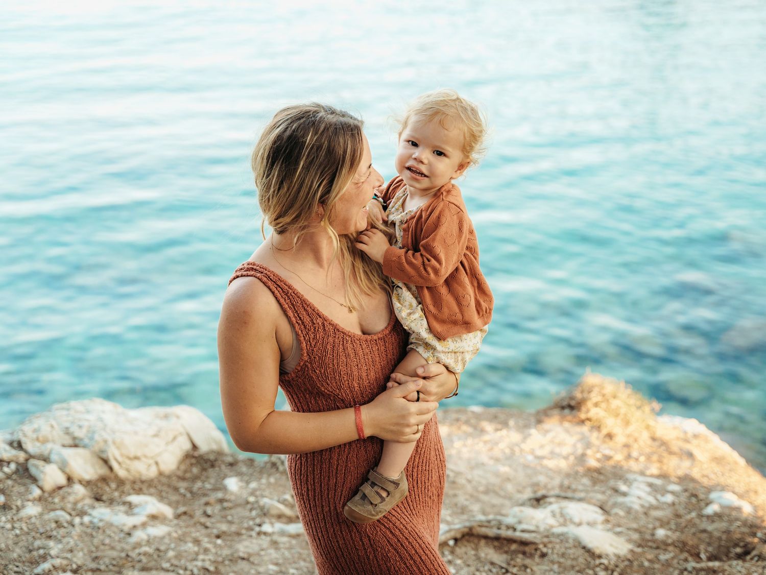 Loving mother holding and kissing her baby by a beautiful turquoise sea.
