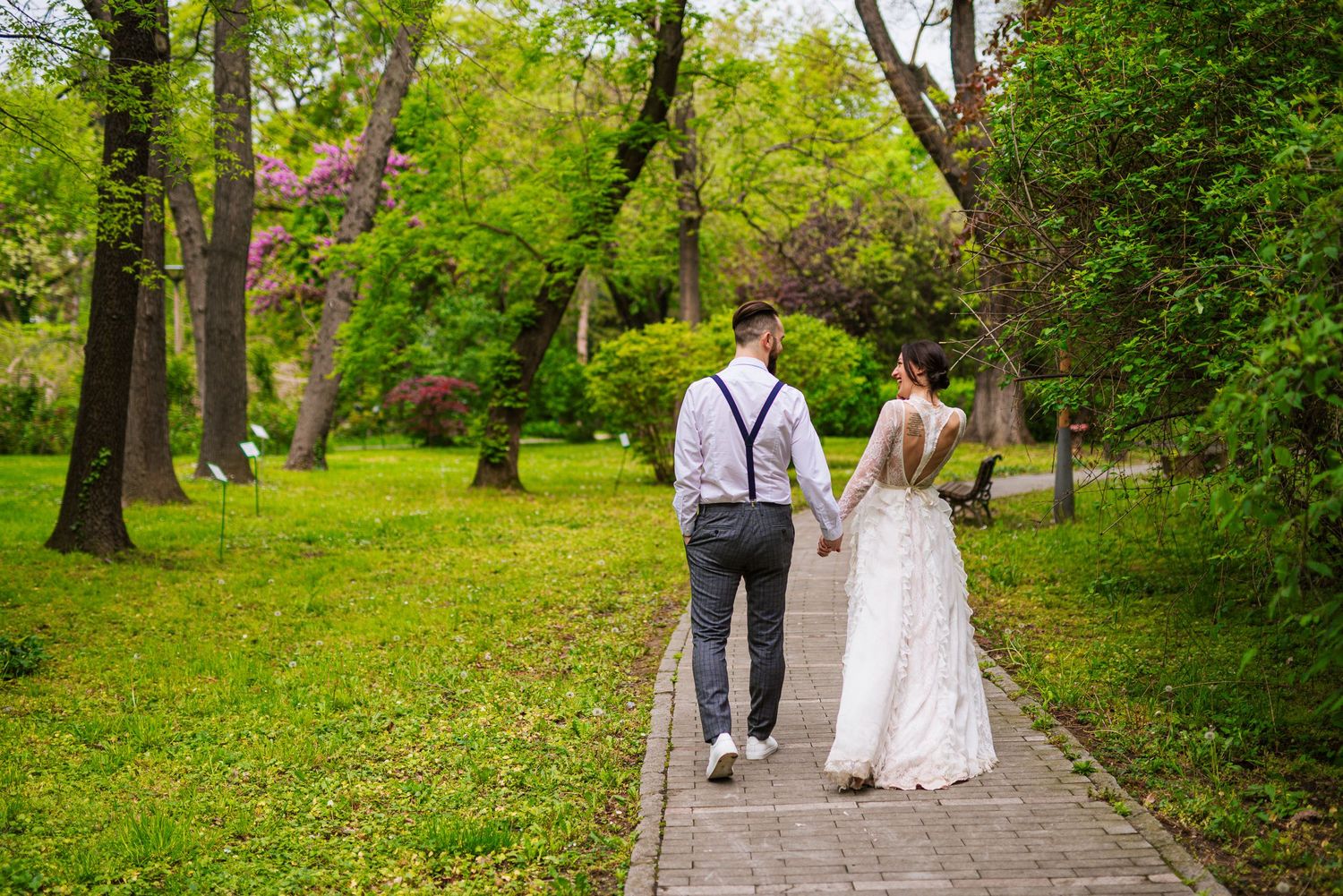 Newlywed couple walks hand in hand down a tree-lined garden path on their wedding day.