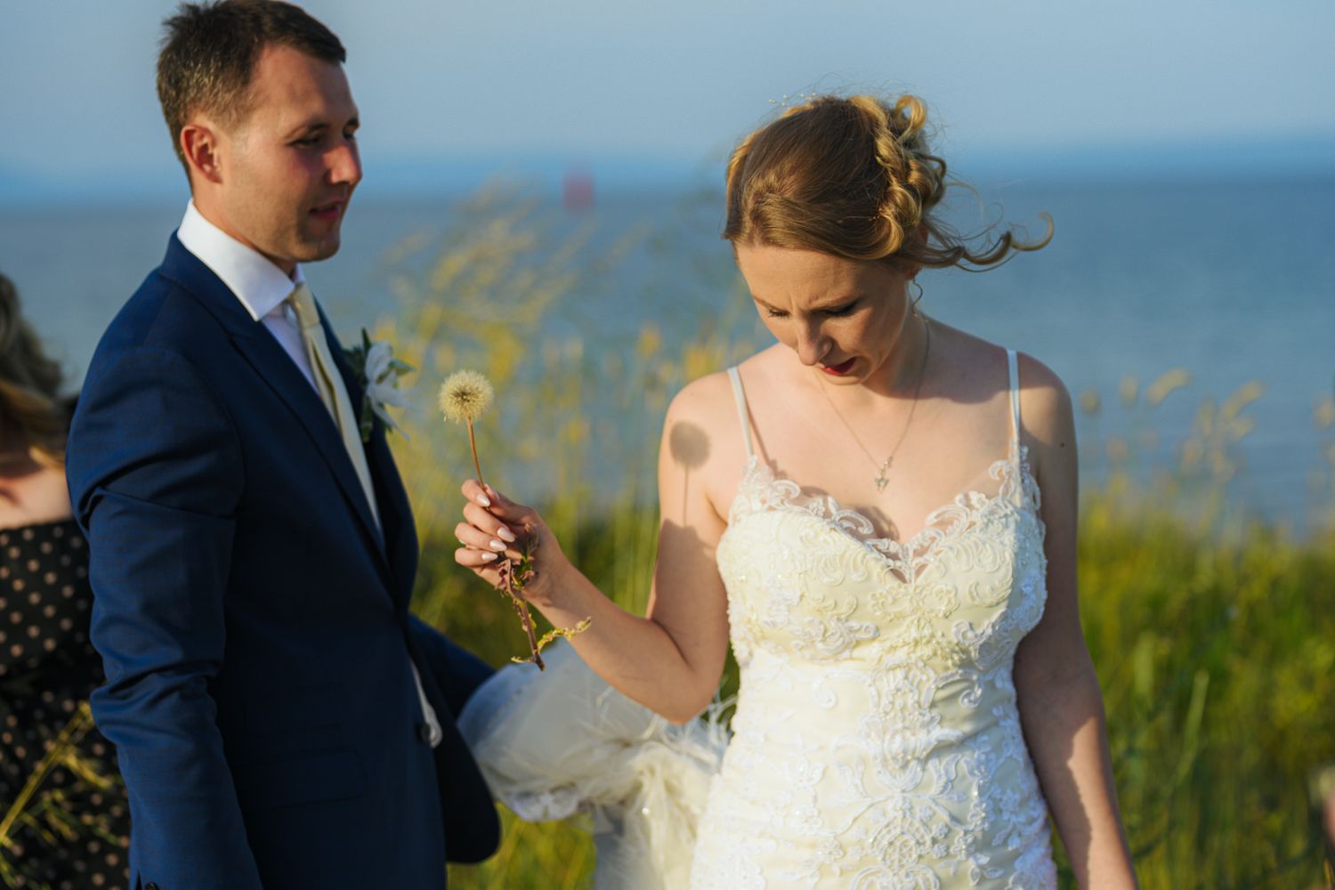 Bride and groom sharing a tender moment outdoors with ocean and wildflowers behind them.