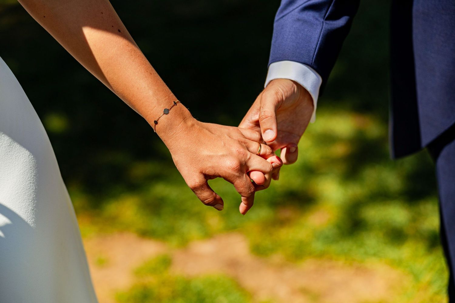 Close-up of bride and groom holding hands at wedding ceremony outdoors.