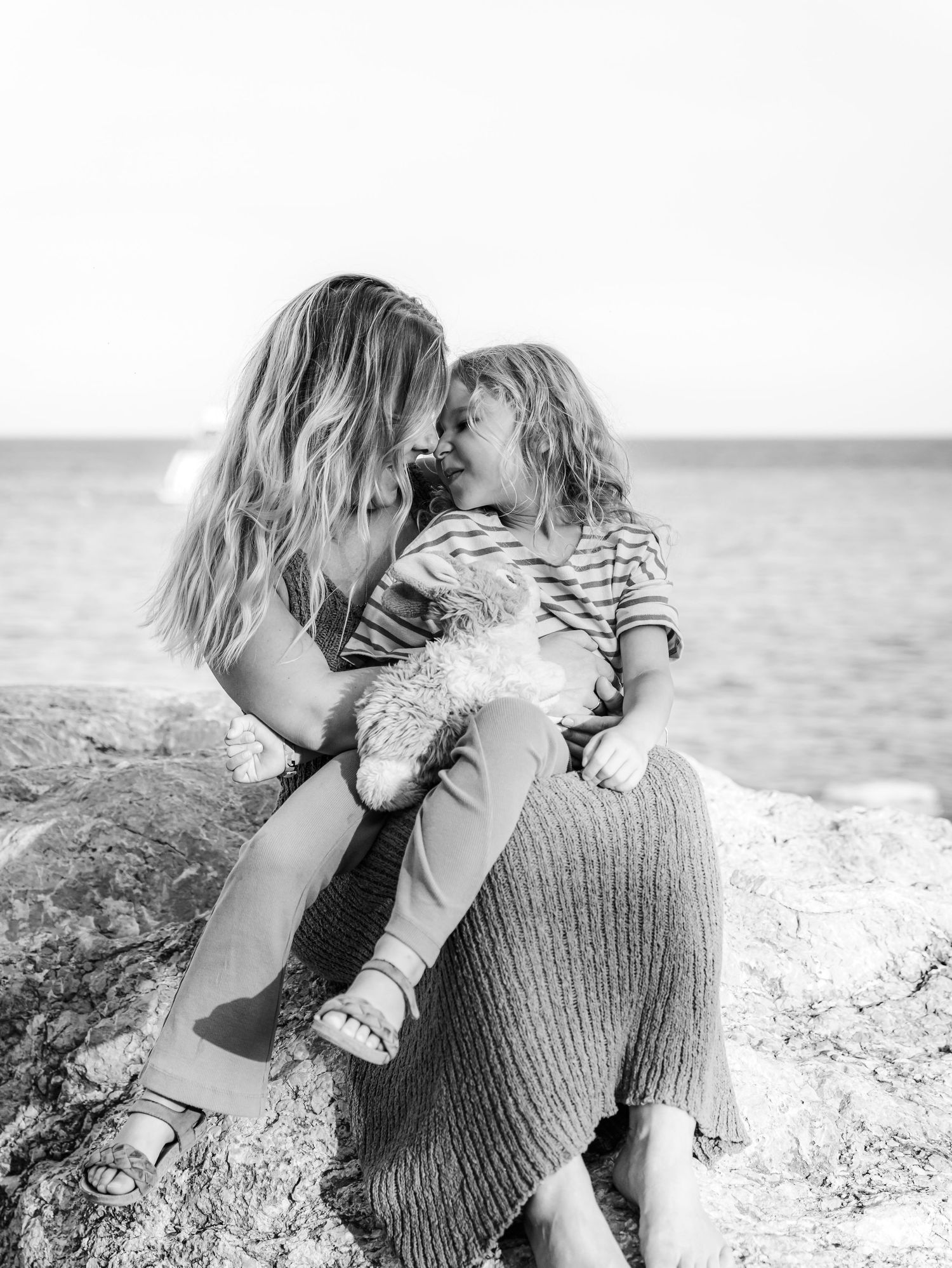 Black and white photo of mother and child sharing sweet moment on rocky beach.
