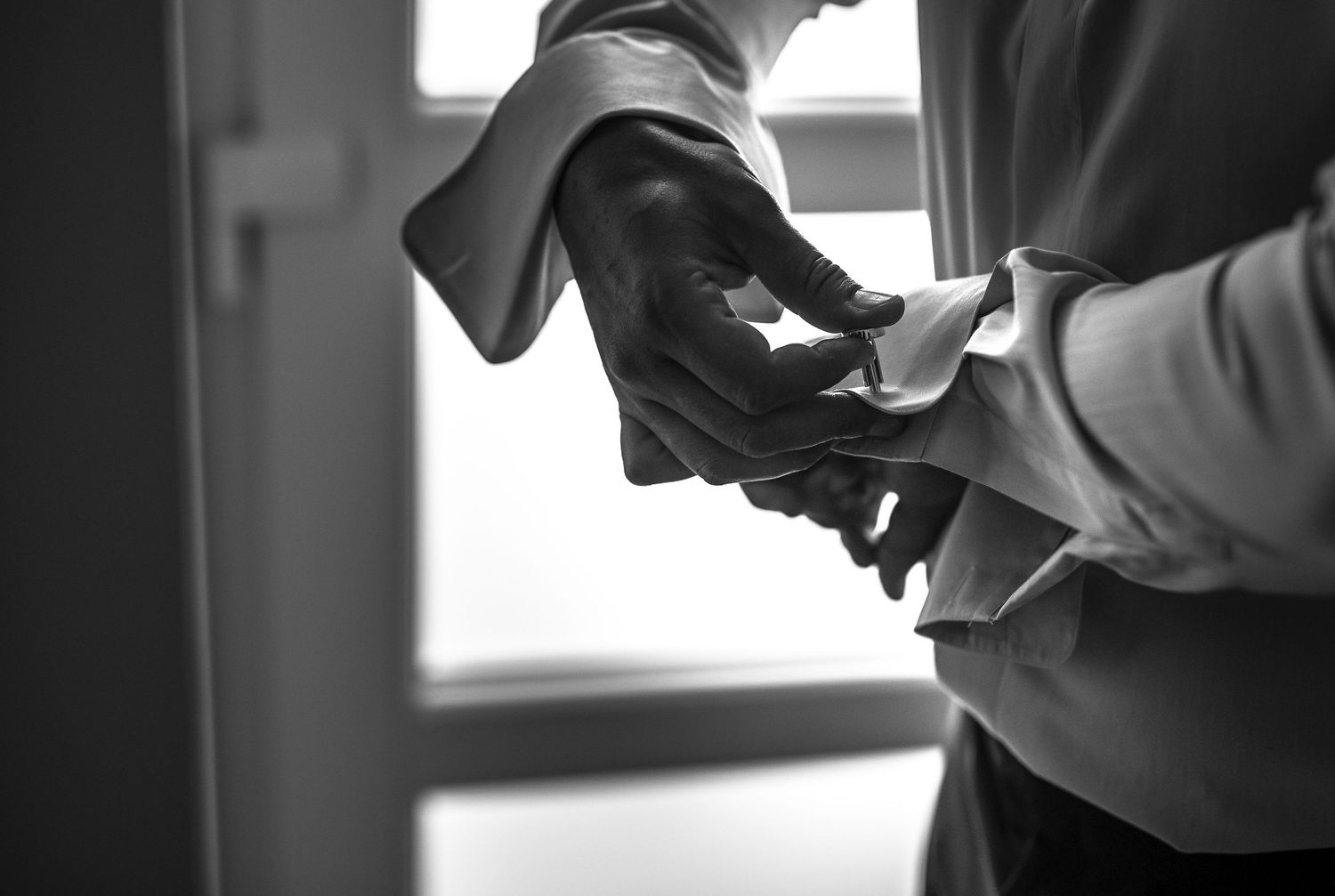 Black and white close-up of a groom fastening his cufflinks while getting dressed for his wedding.
