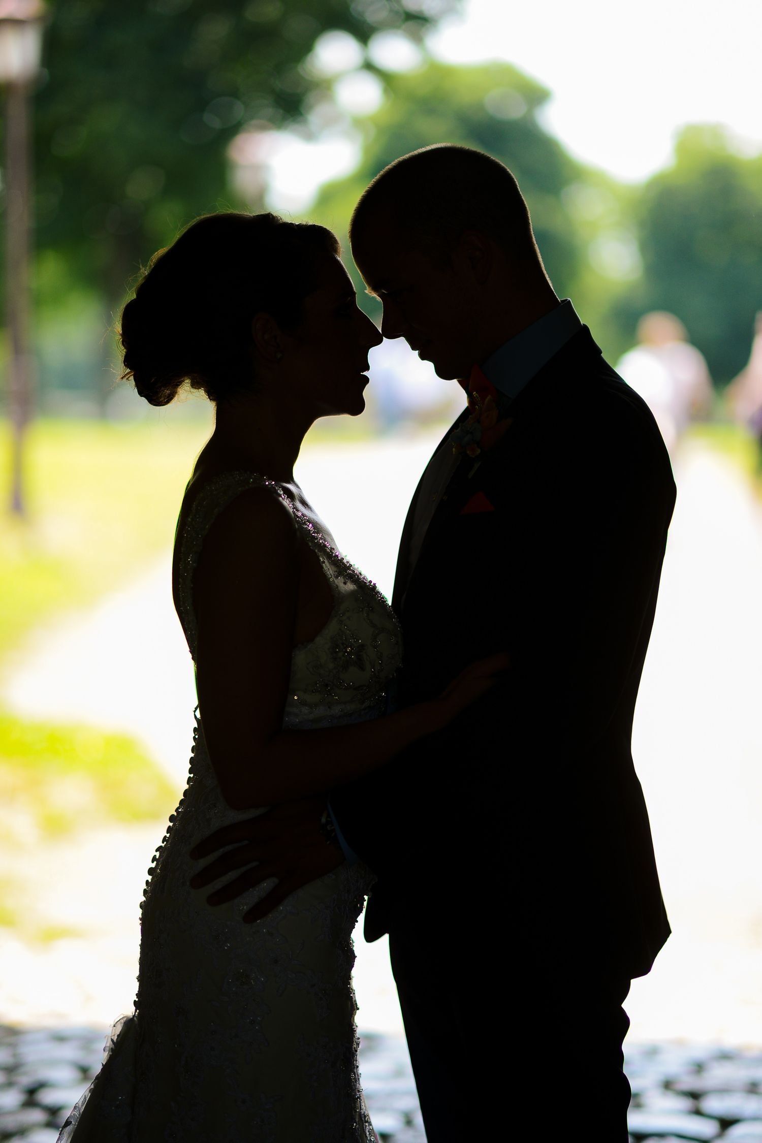 Silhouette of bride and groom facing each other in a tender moment on their wedding day outdoors.