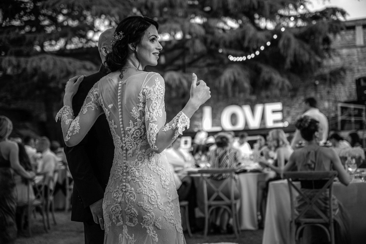 Black and white photo of bride and groom dancing at outdoor reception with LOVE sign behind them.