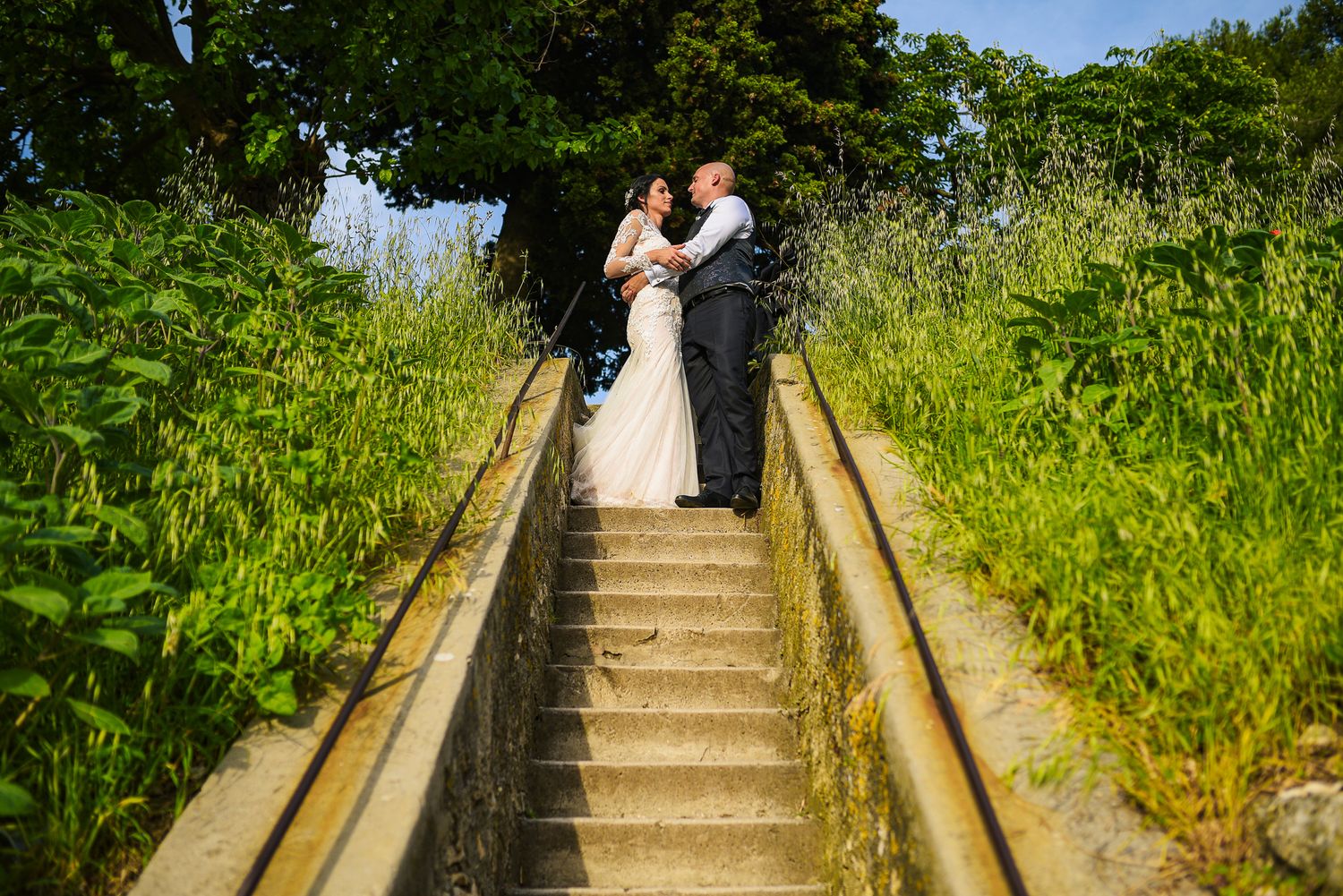 Wedding couple sharing an intimate moment on stone steps surrounded by lush greenery.