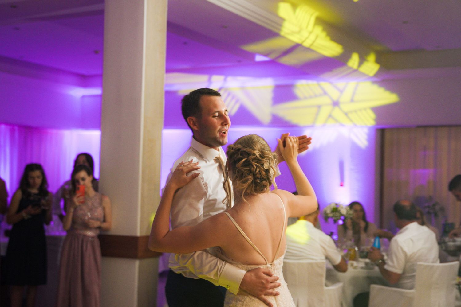 Bride and groom share their first dance under purple and yellow lights at elegant wedding reception.