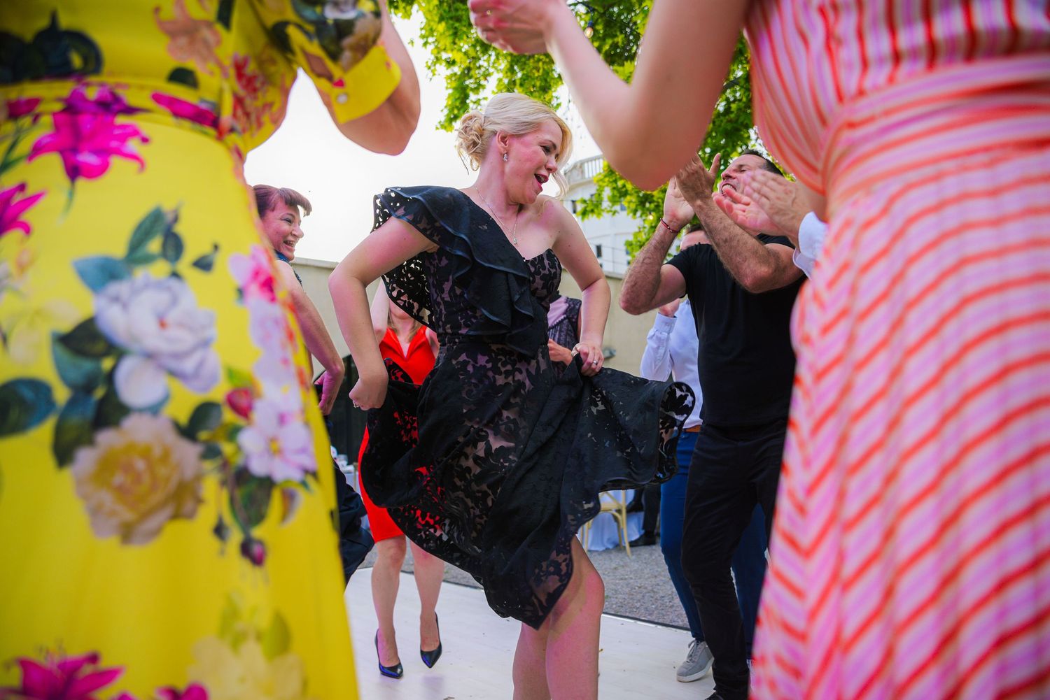 Guests dancing joyfully outdoors at a wedding reception in colorful floral dresses.