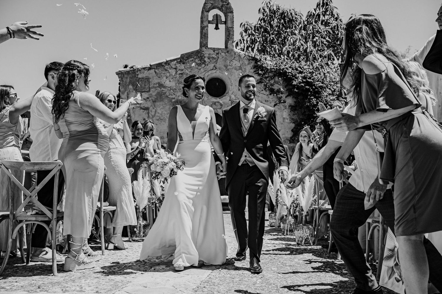 Black and white photo of bride and groom walking down aisle as guests celebrate with confetti.