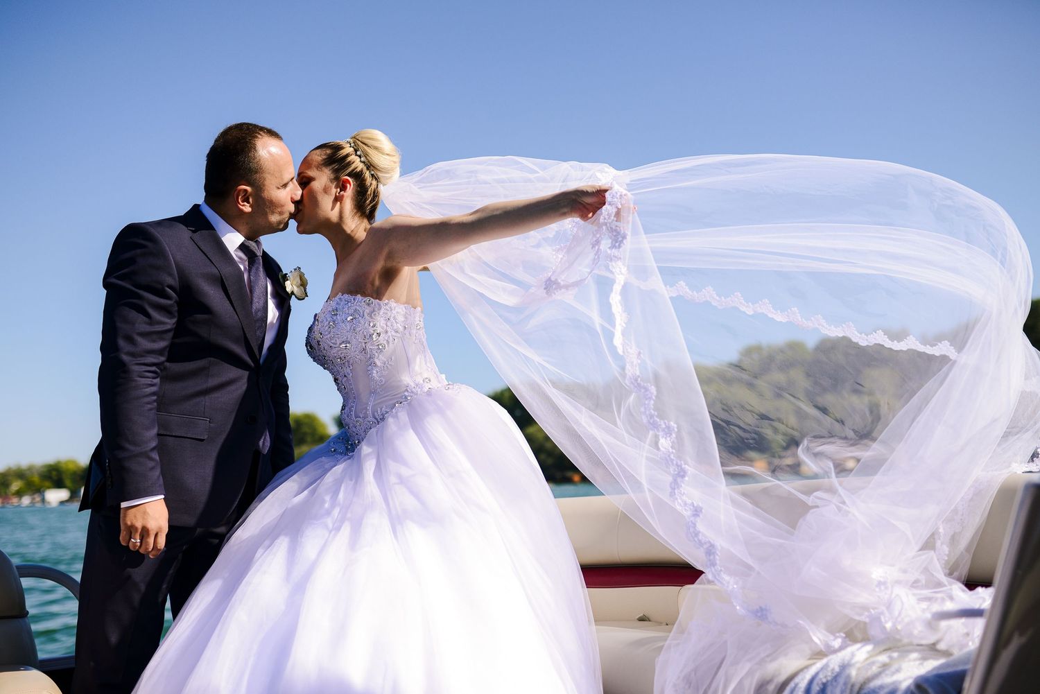 Bride and groom kissing on a boat with her elegant white ballgown veil flowing in the ocean breeze.