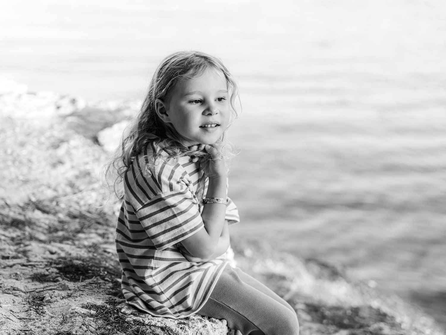 Black and white photo of a young girl sitting on rocks near the ocean.